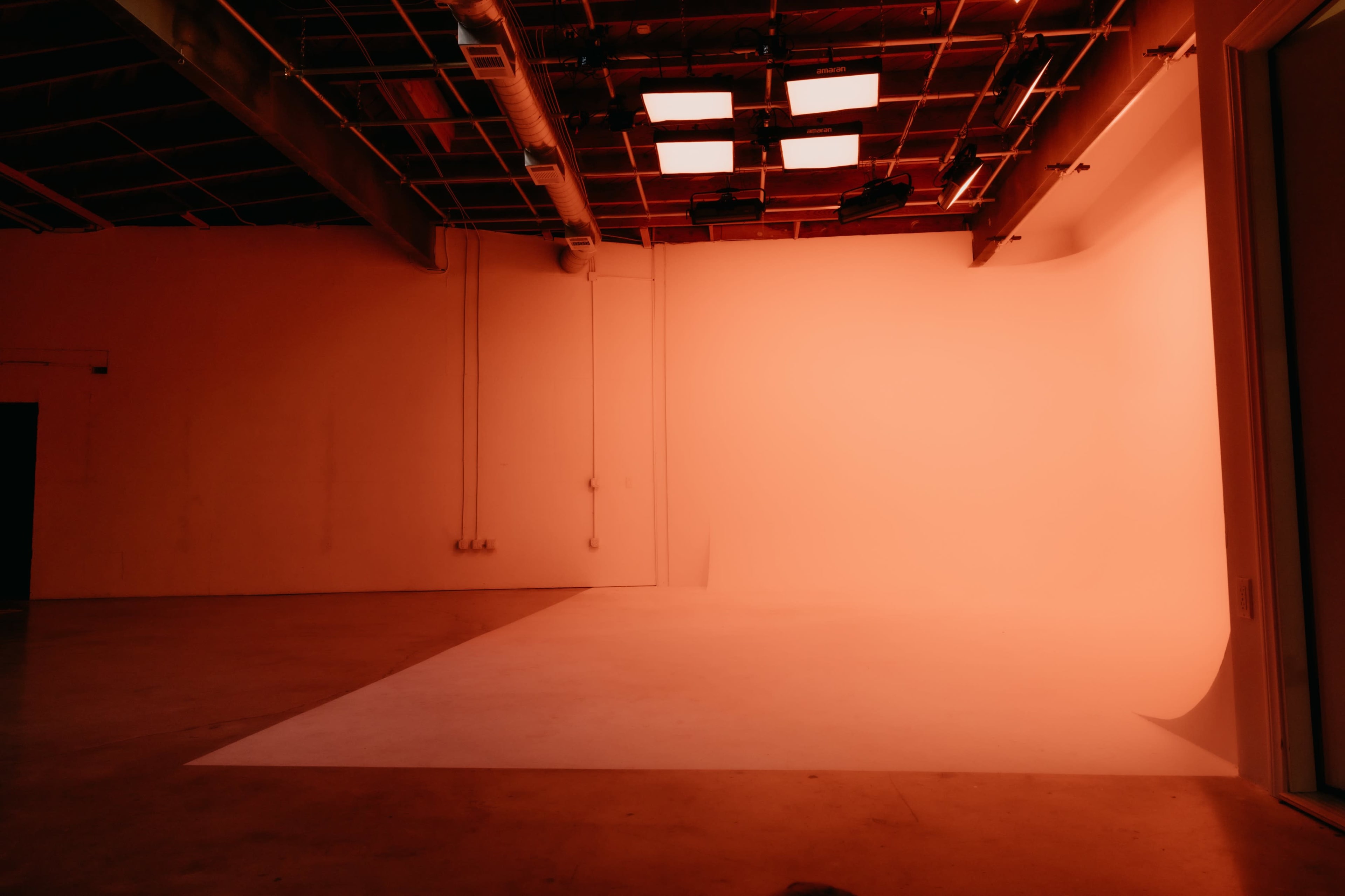 The image shows a minimalist studio space with a smooth, illuminated backdrop and overhead lights.