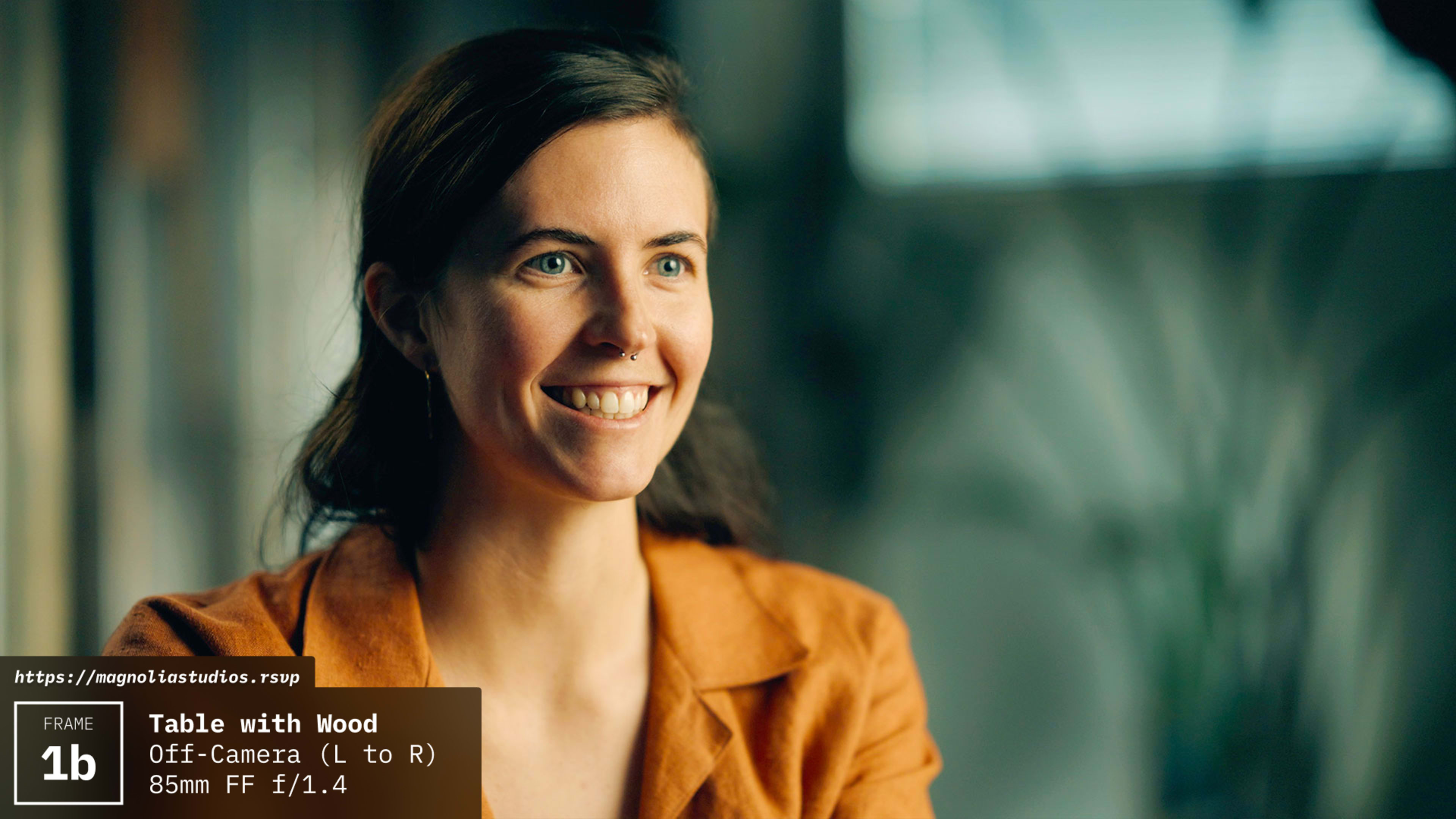 A woman with dark hair smiles while seated at a wooden table.