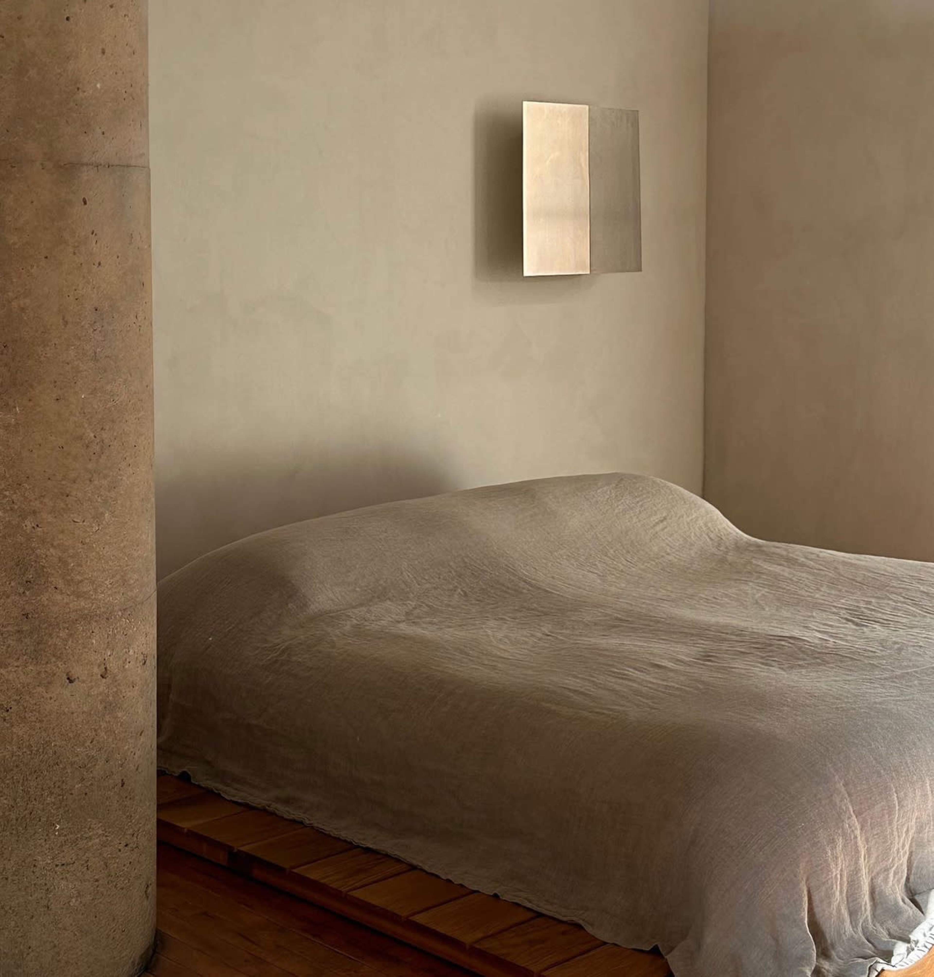 A minimalistic bedroom features a simple bed covered with a textured blanket and a small mirror hanging on the wall.