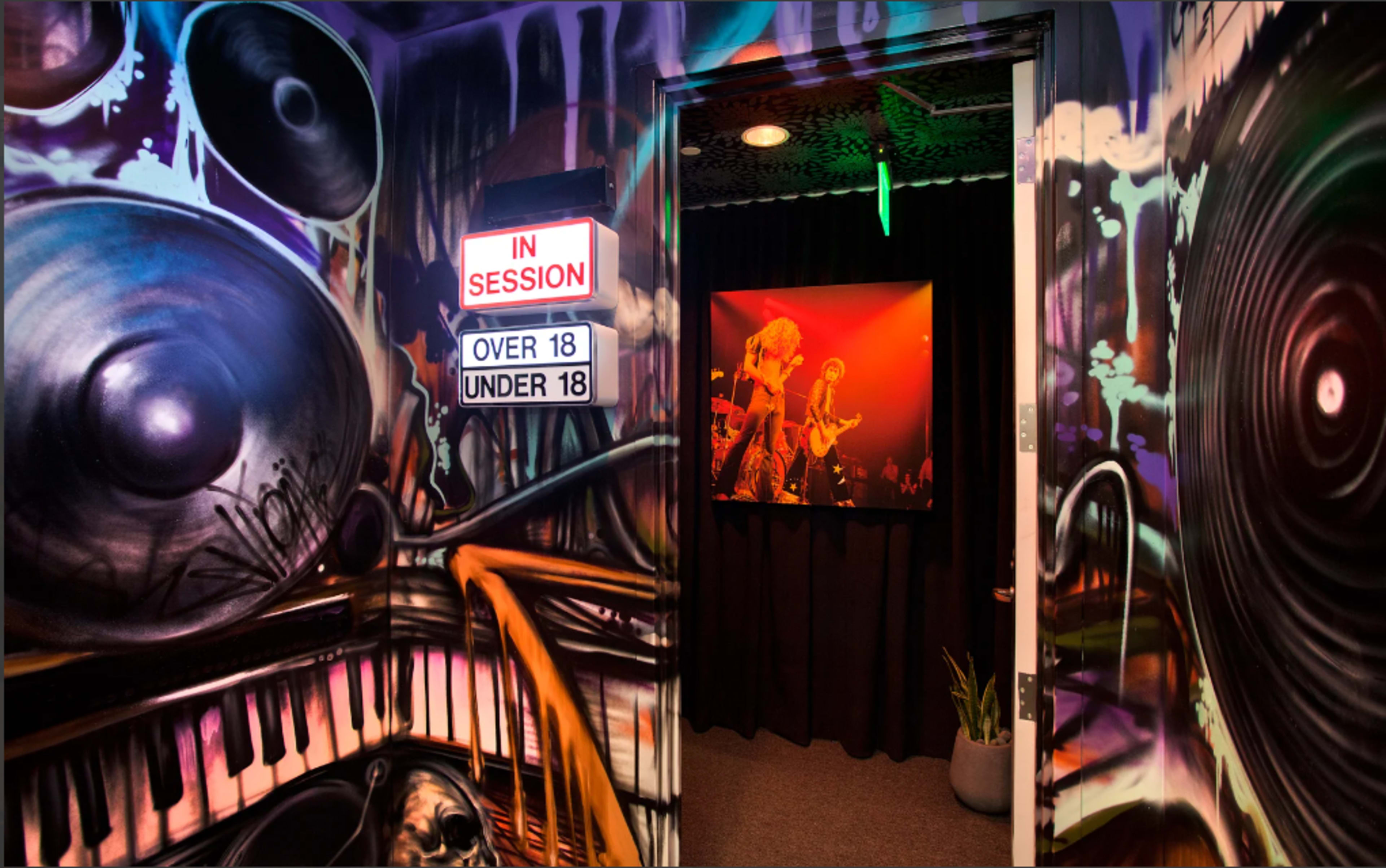A hallway features vibrant graffiti art of speakers and a piano, with a sign indicating "IN SESSION" and a doorway leading to a performance area.