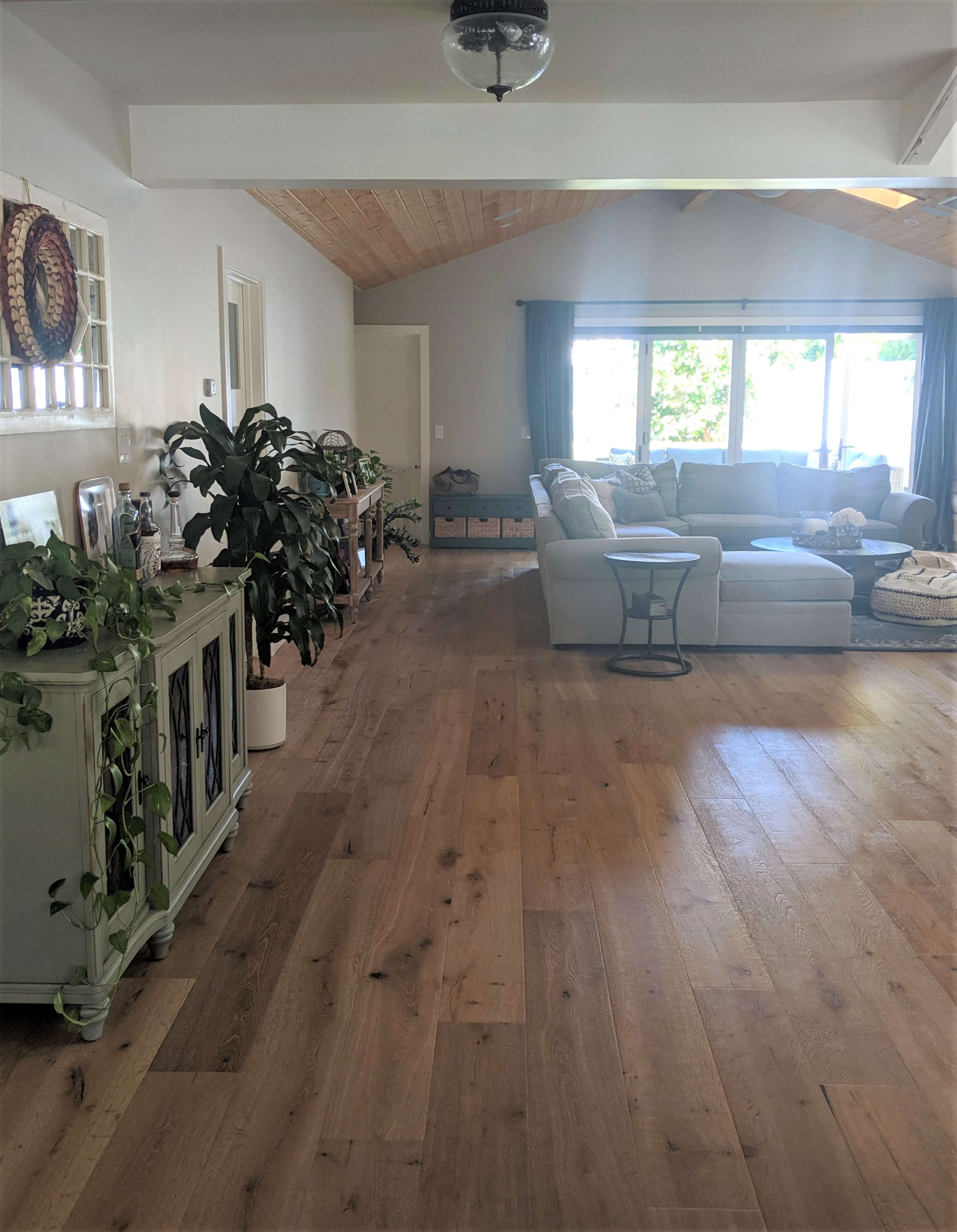 A spacious living room with wooden flooring, a light-colored sofa, and large windows letting in natural light.