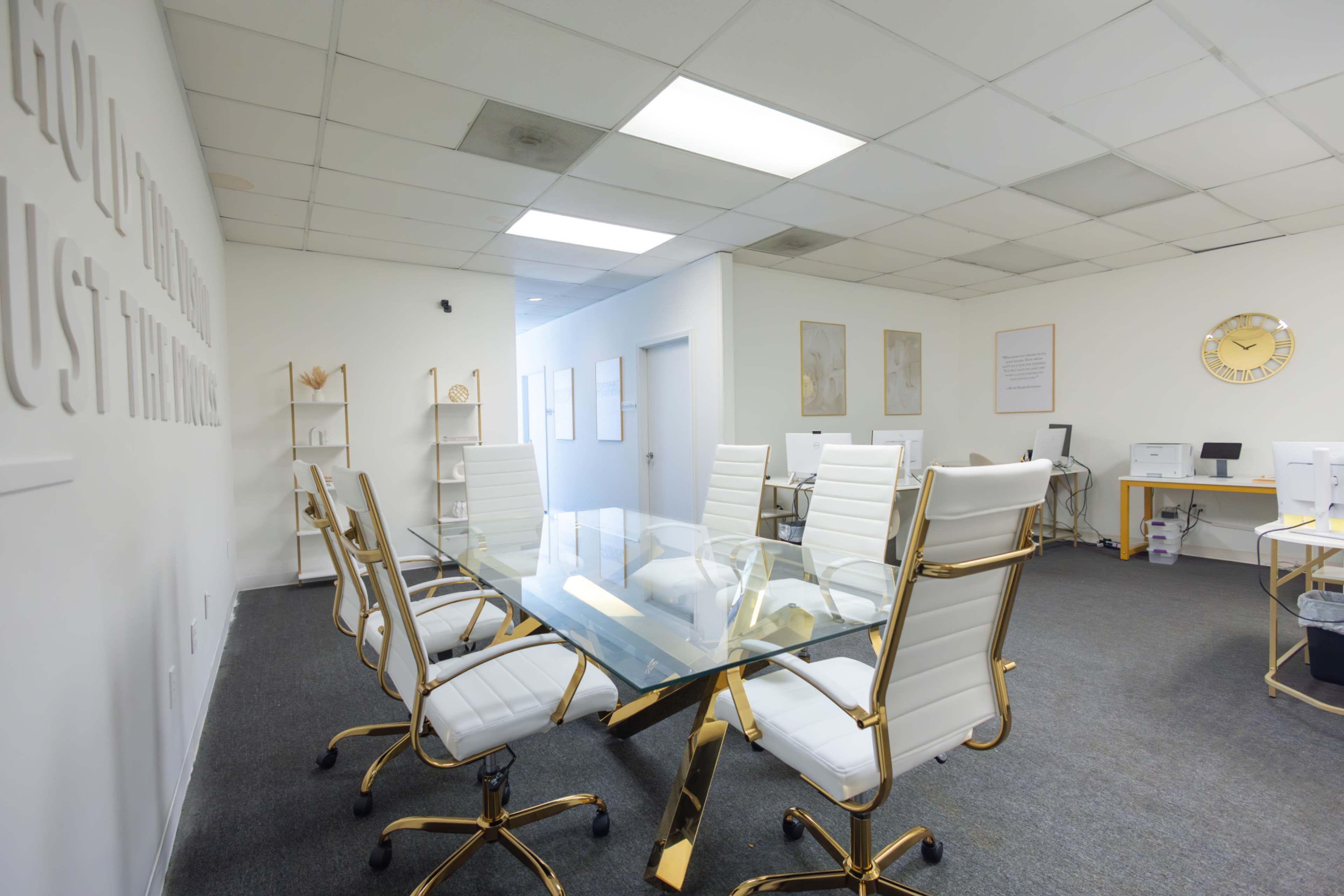 The image shows a modern office meeting room with a glass table surrounded by white ergonomic chairs and a minimalist design.