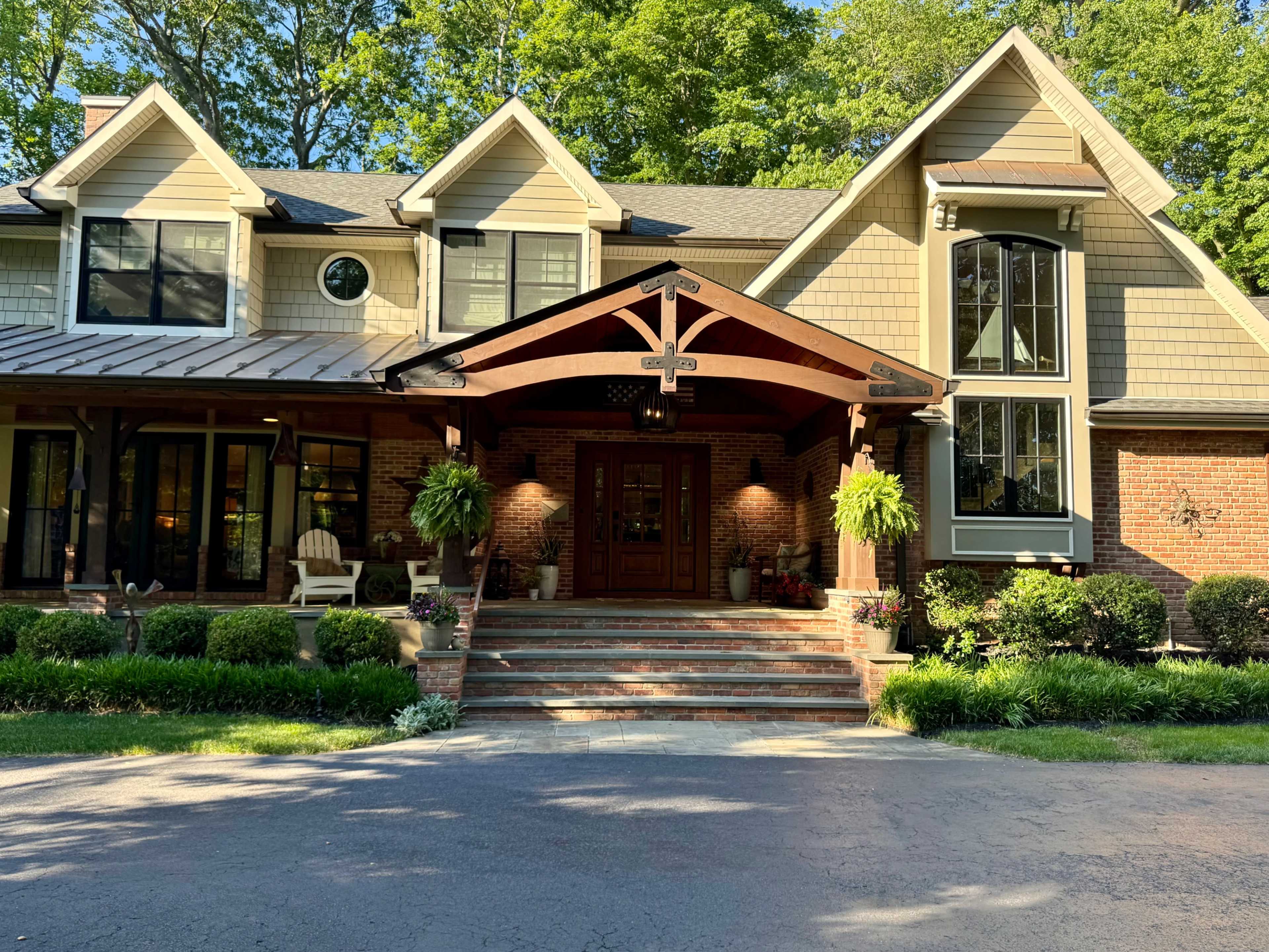 The image shows a large, stylish house with a covered entrance, surrounded by well-maintained landscaping and steps leading to the front door.