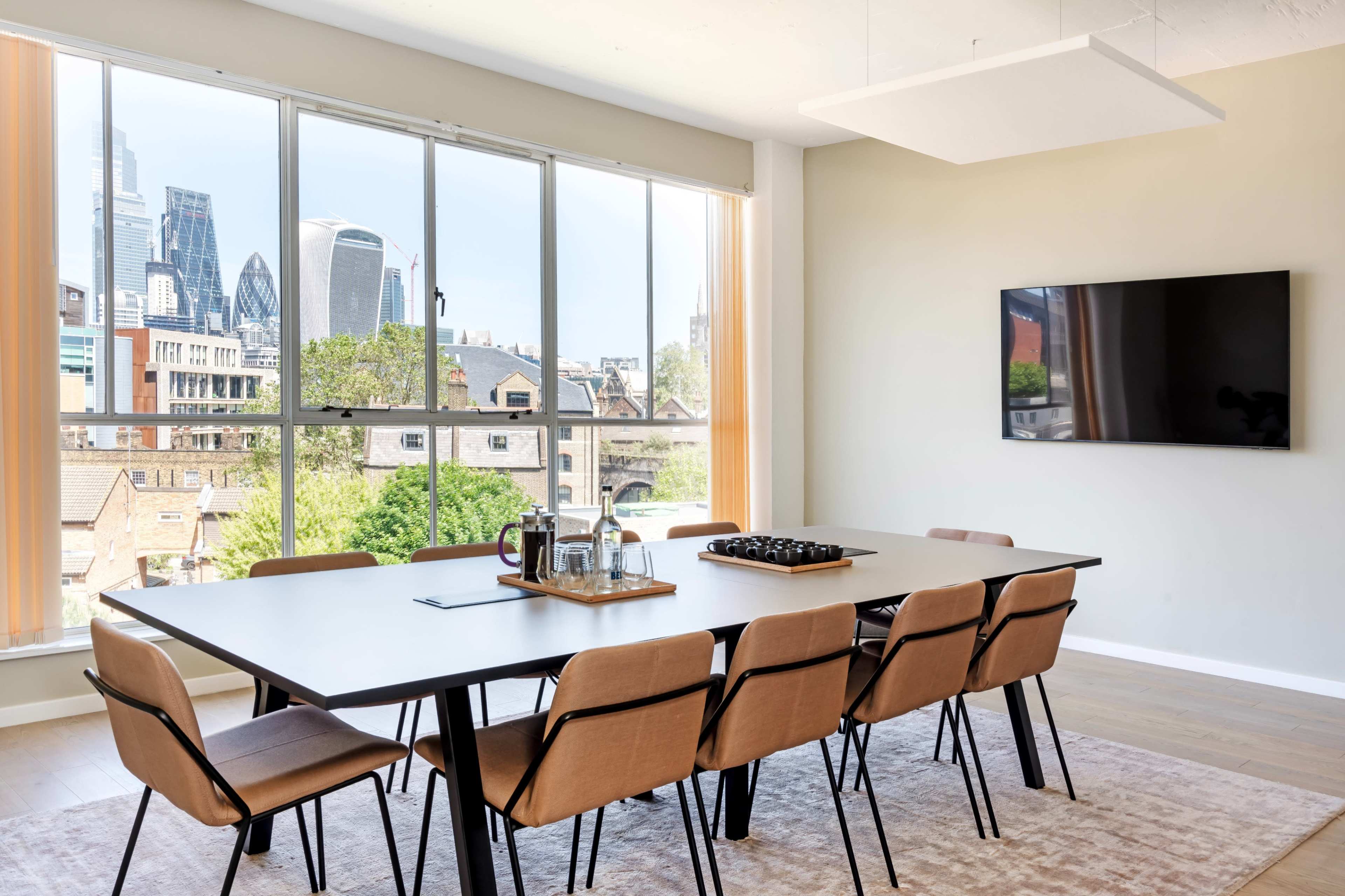 A modern conference room features a large table surrounded by chairs, with floor-to-ceiling windows showing a city skyline.