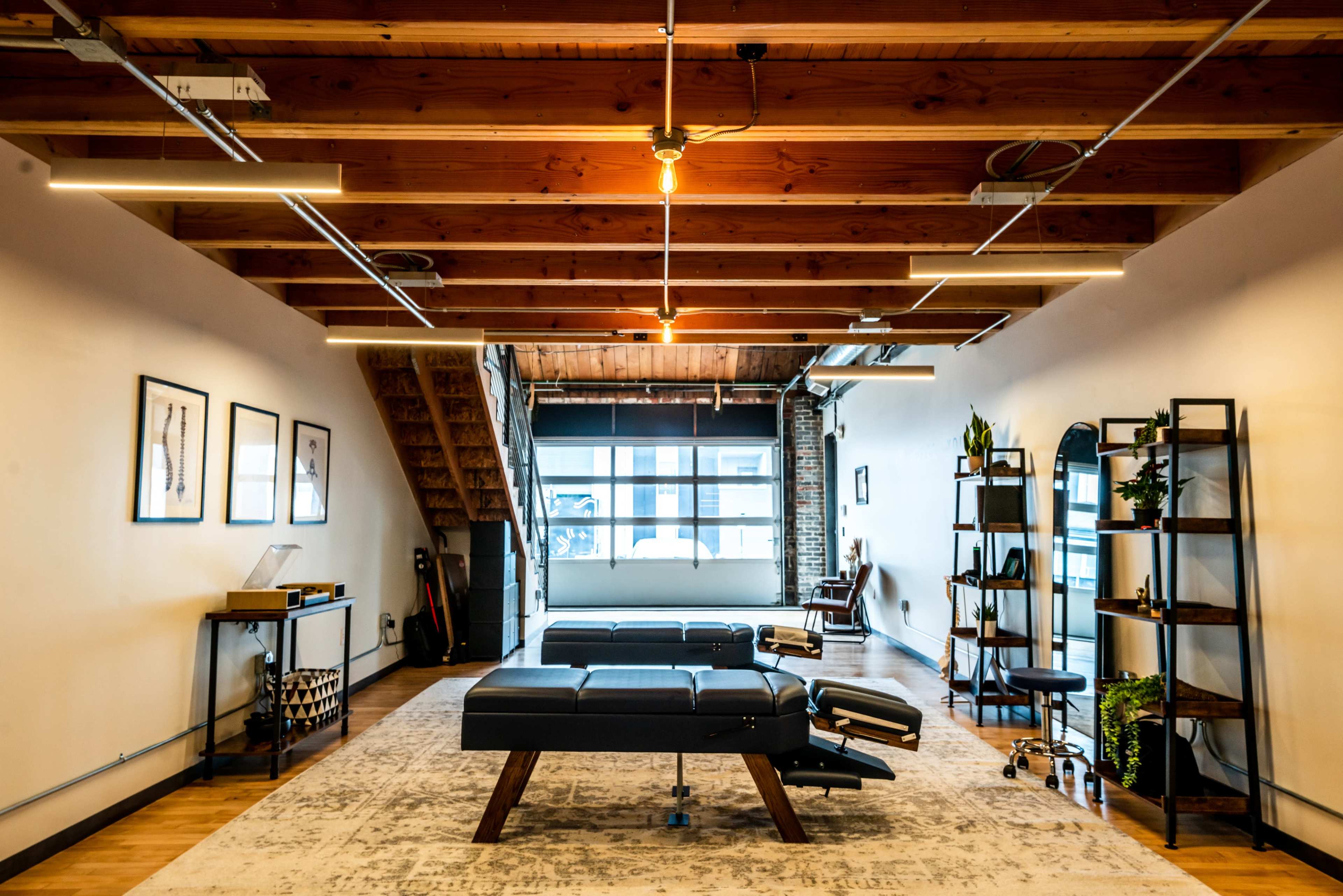 A spacious, modern room with wooden beams, large windows, two gray couches, and a bookshelf against the wall.