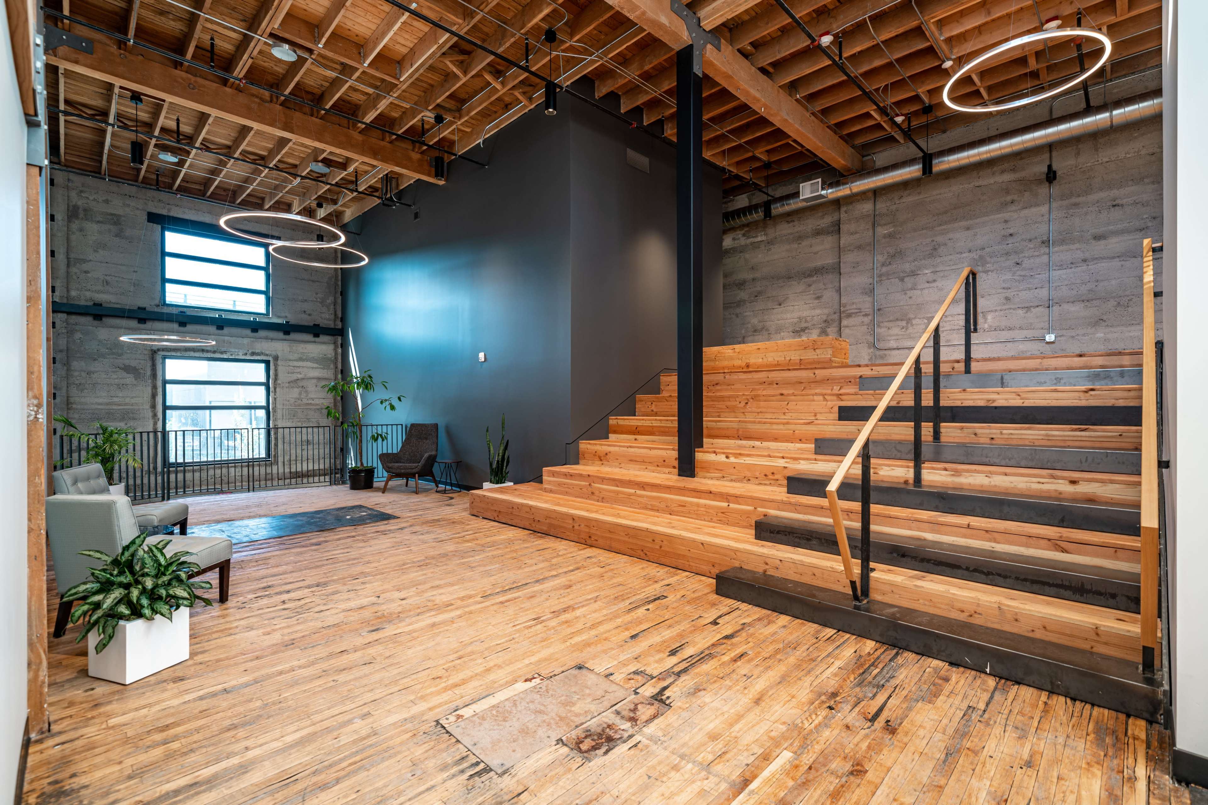 A modern interior with wooden stairs leading to a second level, large windows, and a clean, open space featuring minimal furniture and plants.