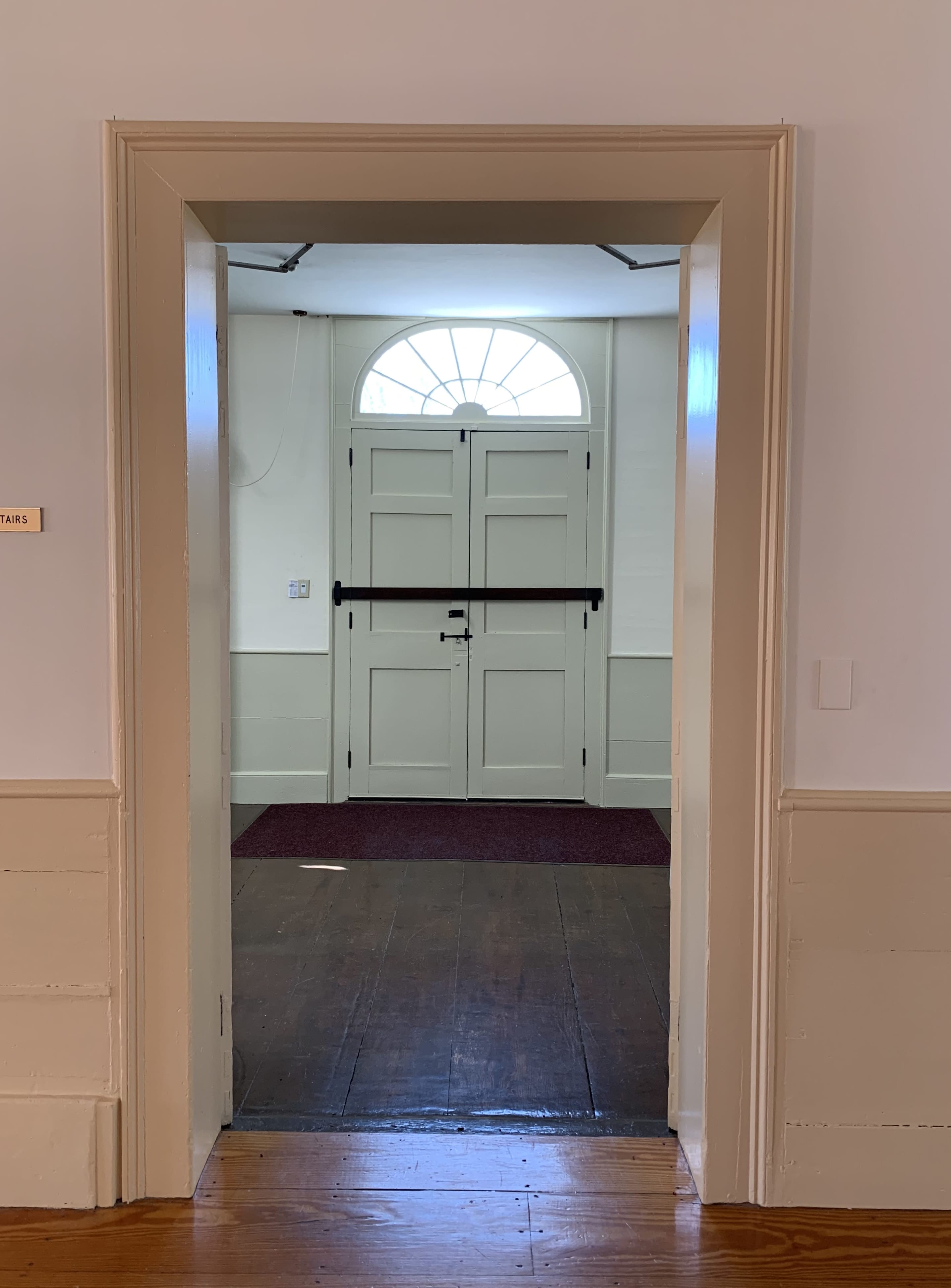 An interior doorway leading to a light-filled entrance with a large arched window above a set of double doors.