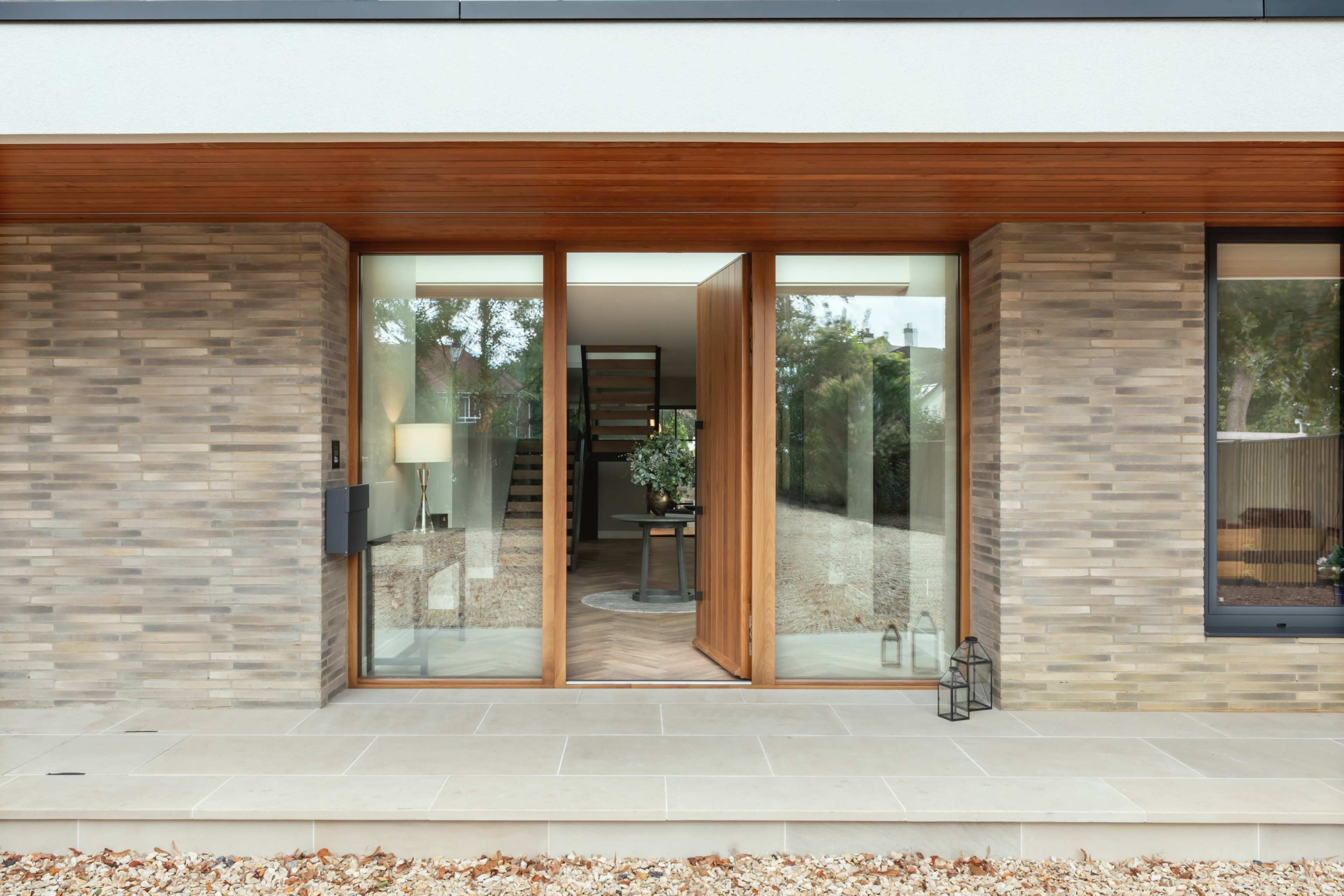 A modern entrance with double wooden doors, flanked by a stone facade, leading to an interior with visible decorations and a staircase.