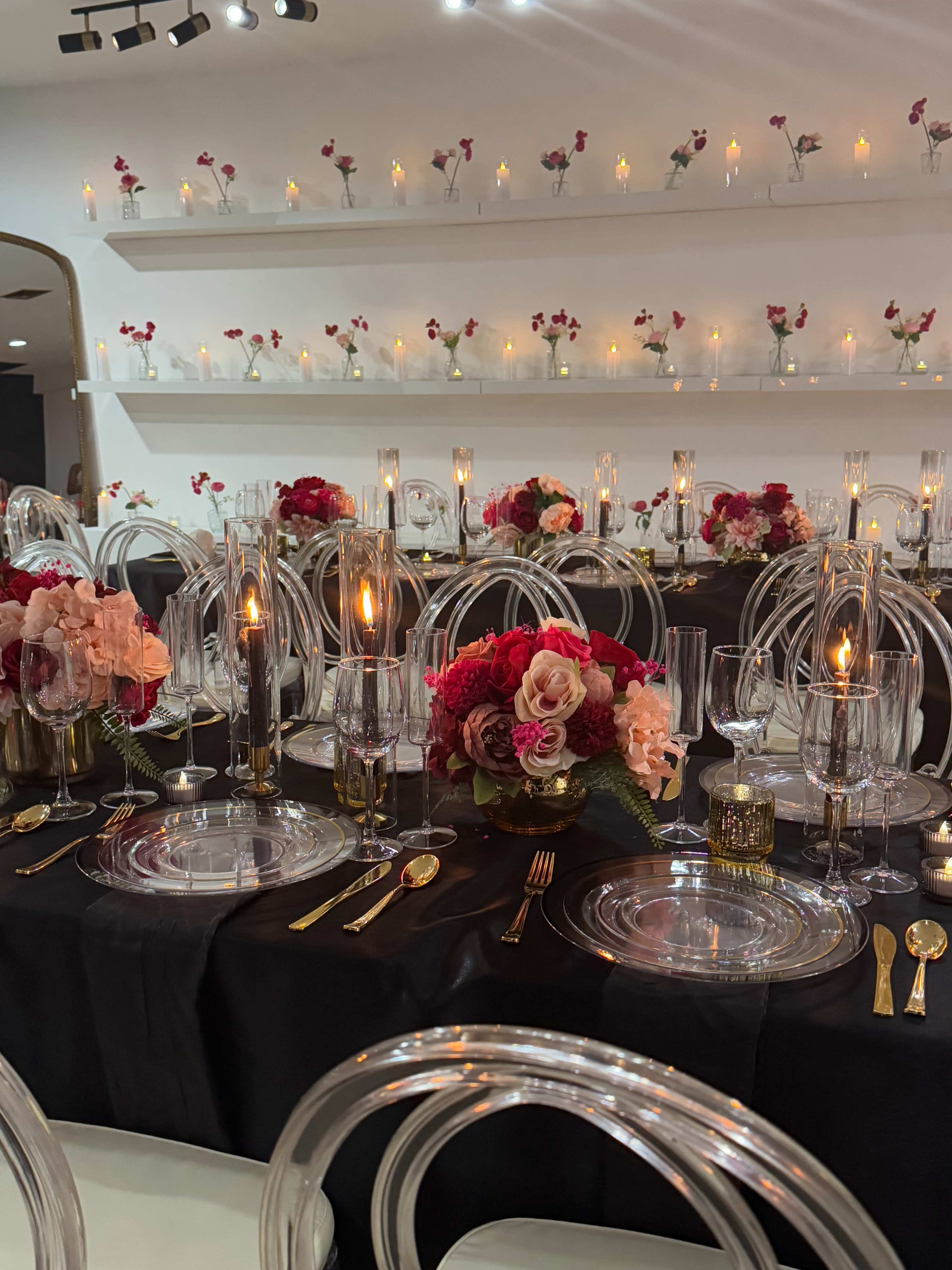 A decorated dining table features elegant glassware, floral centerpieces, and lit candles against a dark tablecloth.