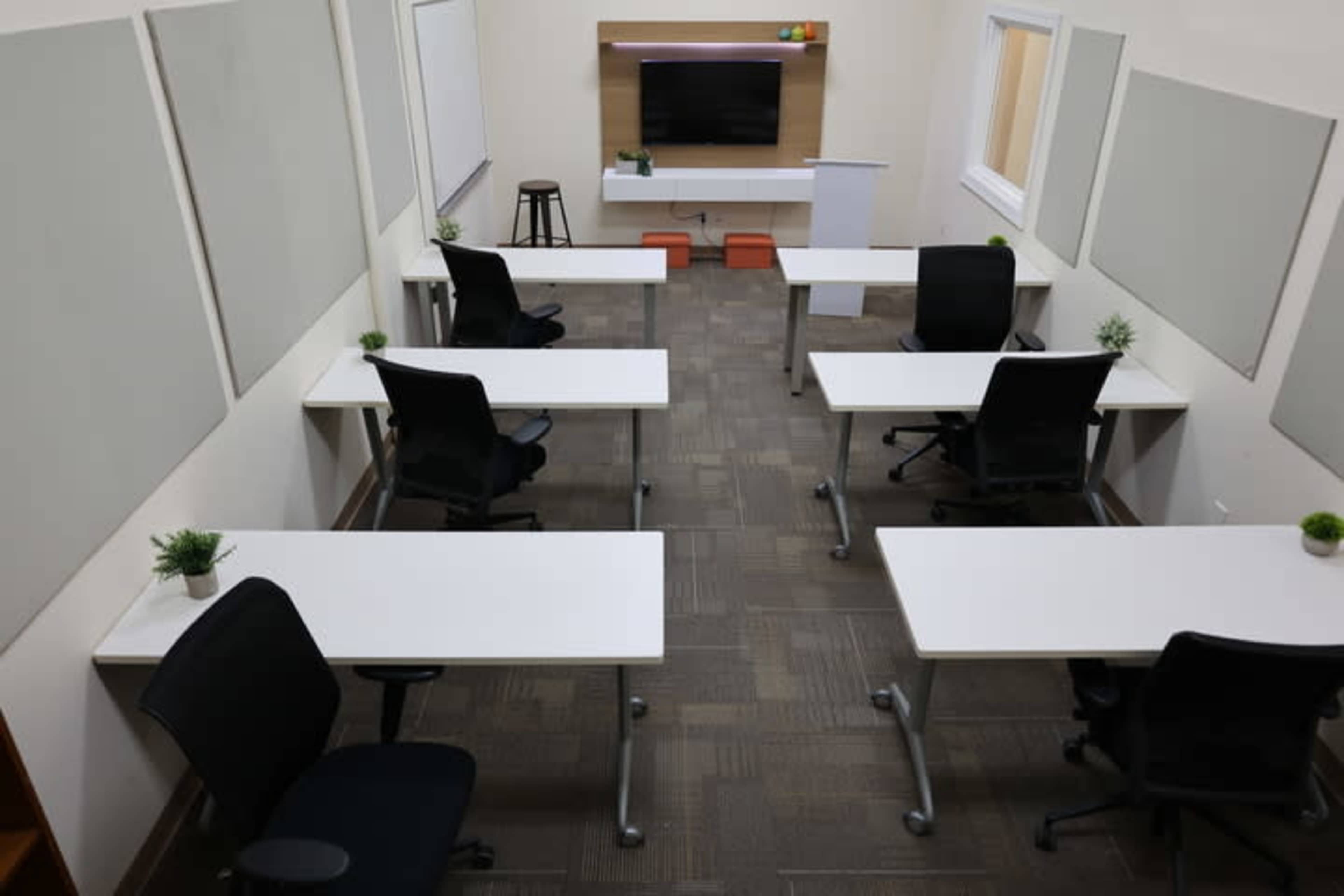 A modern classroom or meeting room featuring several desks with chairs arranged around a central television and presentation area.