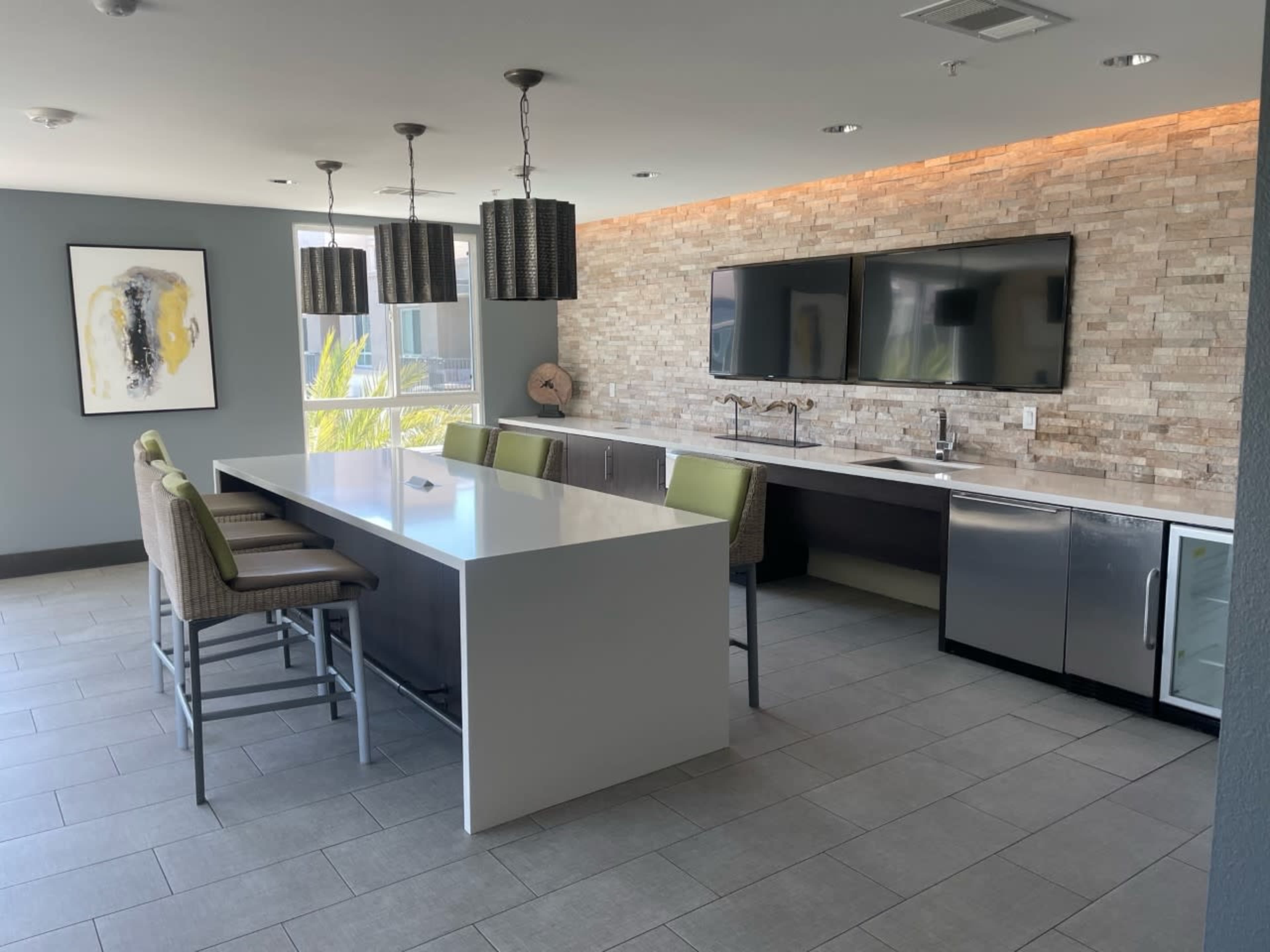 A modern kitchen with a large island, stainless steel appliances, and stone-tiled walls, featuring four green bar stools.