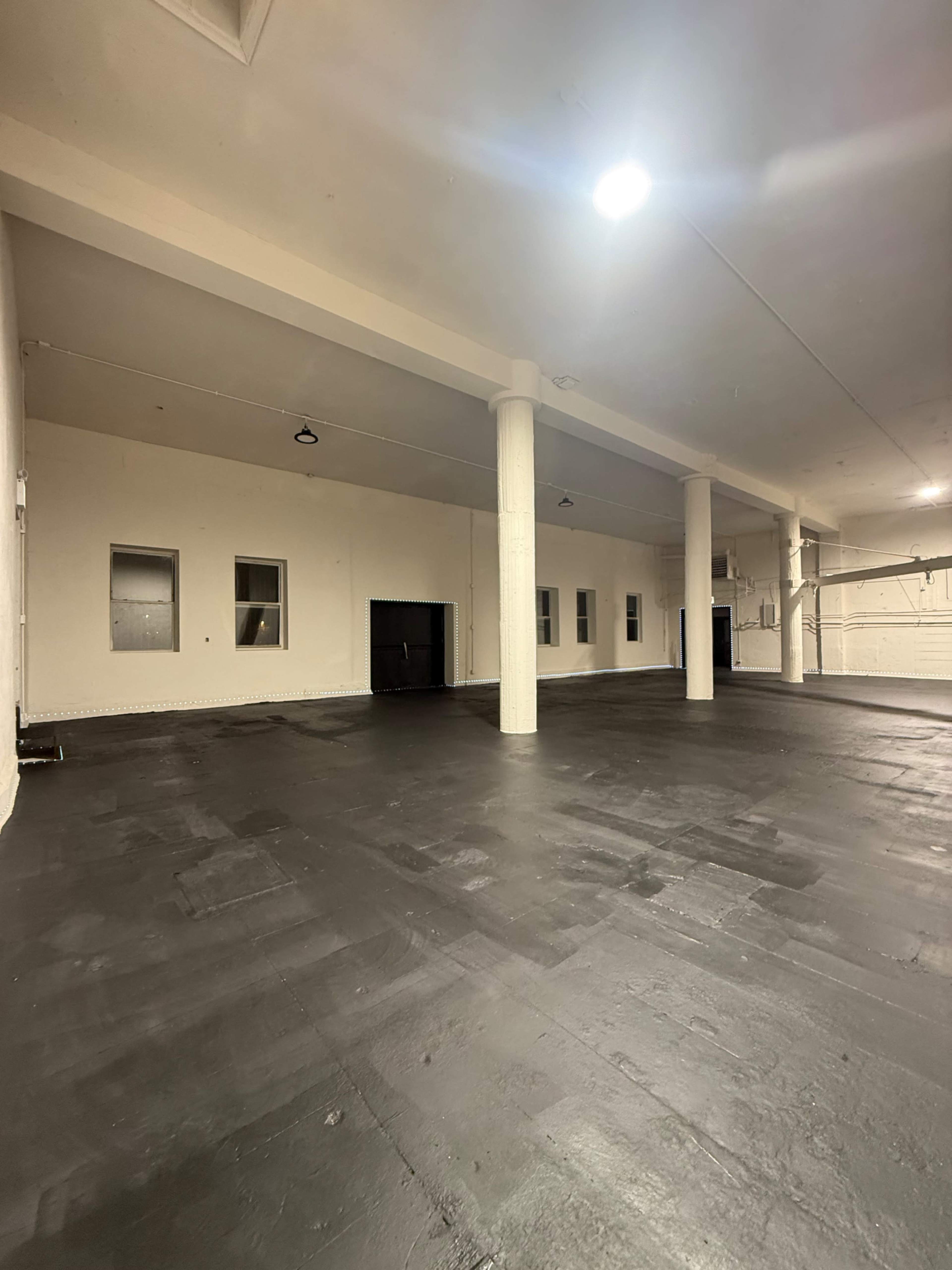 The image shows an empty, large indoor space with a black concrete floor and white walls.