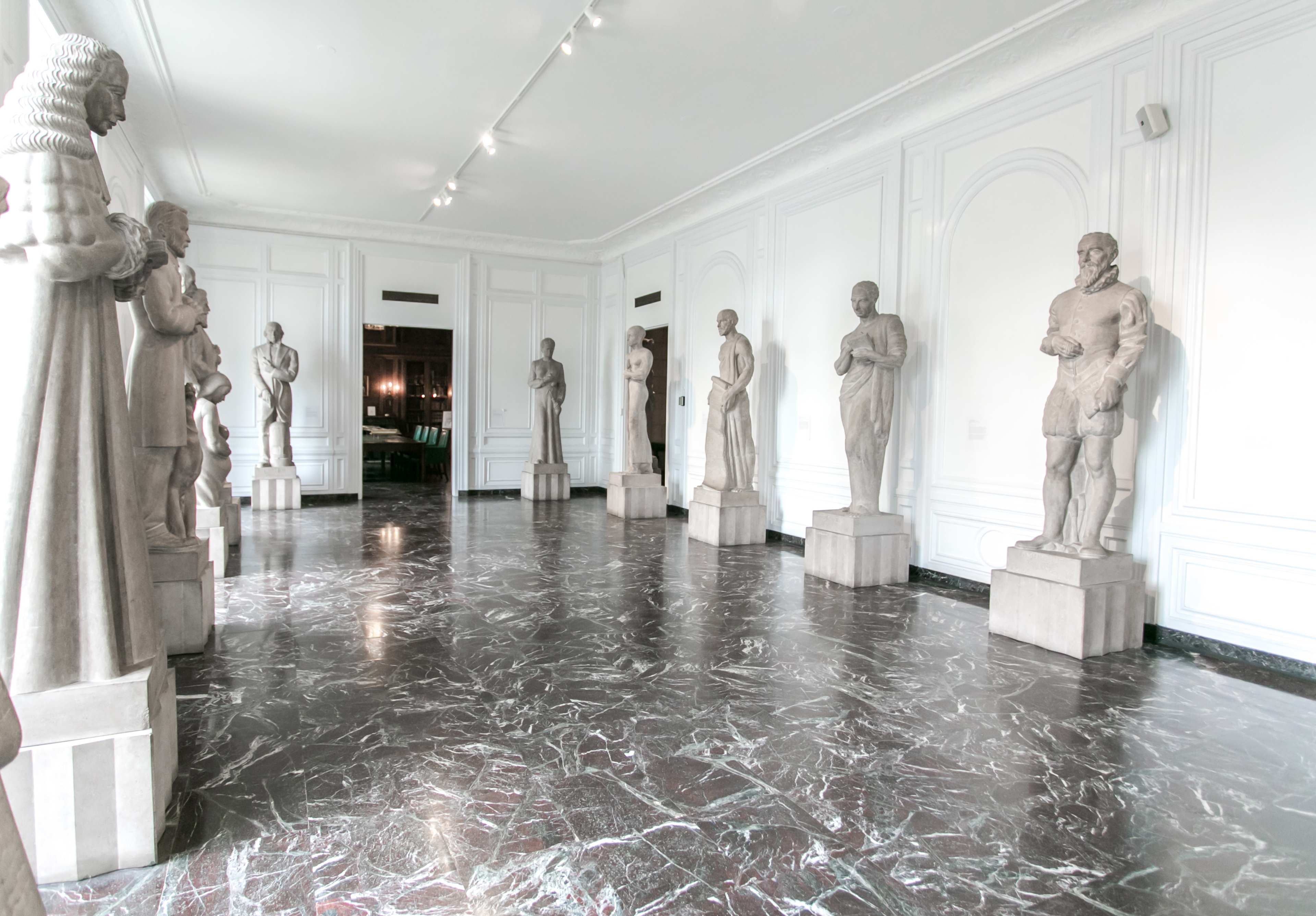 A gallery room lined with several statues on pedestals, arranged symmetrically along the walls.