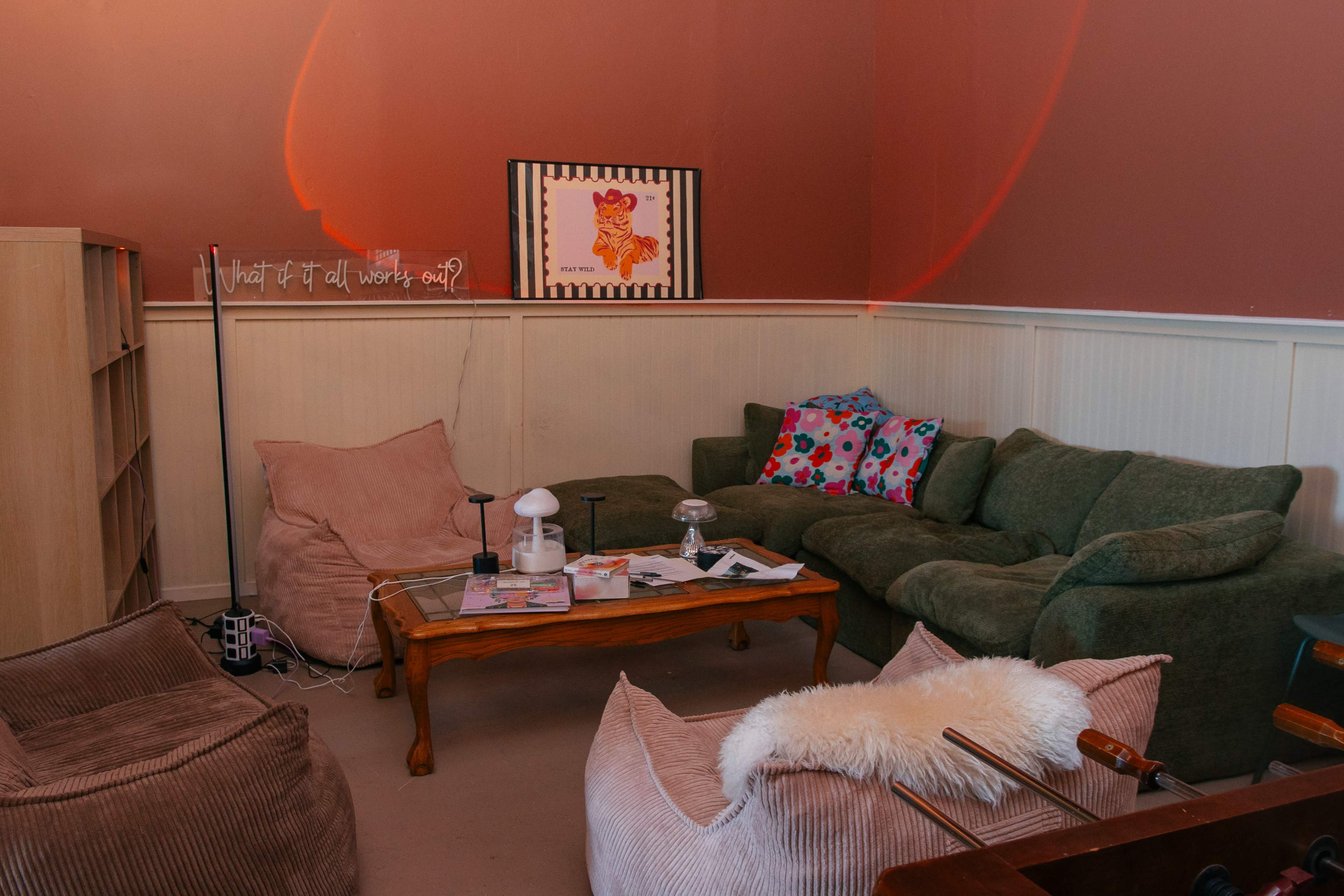 The image shows a cozy living room with a green couch, several bean bags, a coffee table cluttered with magazines, and a framed piece of art on the wall.