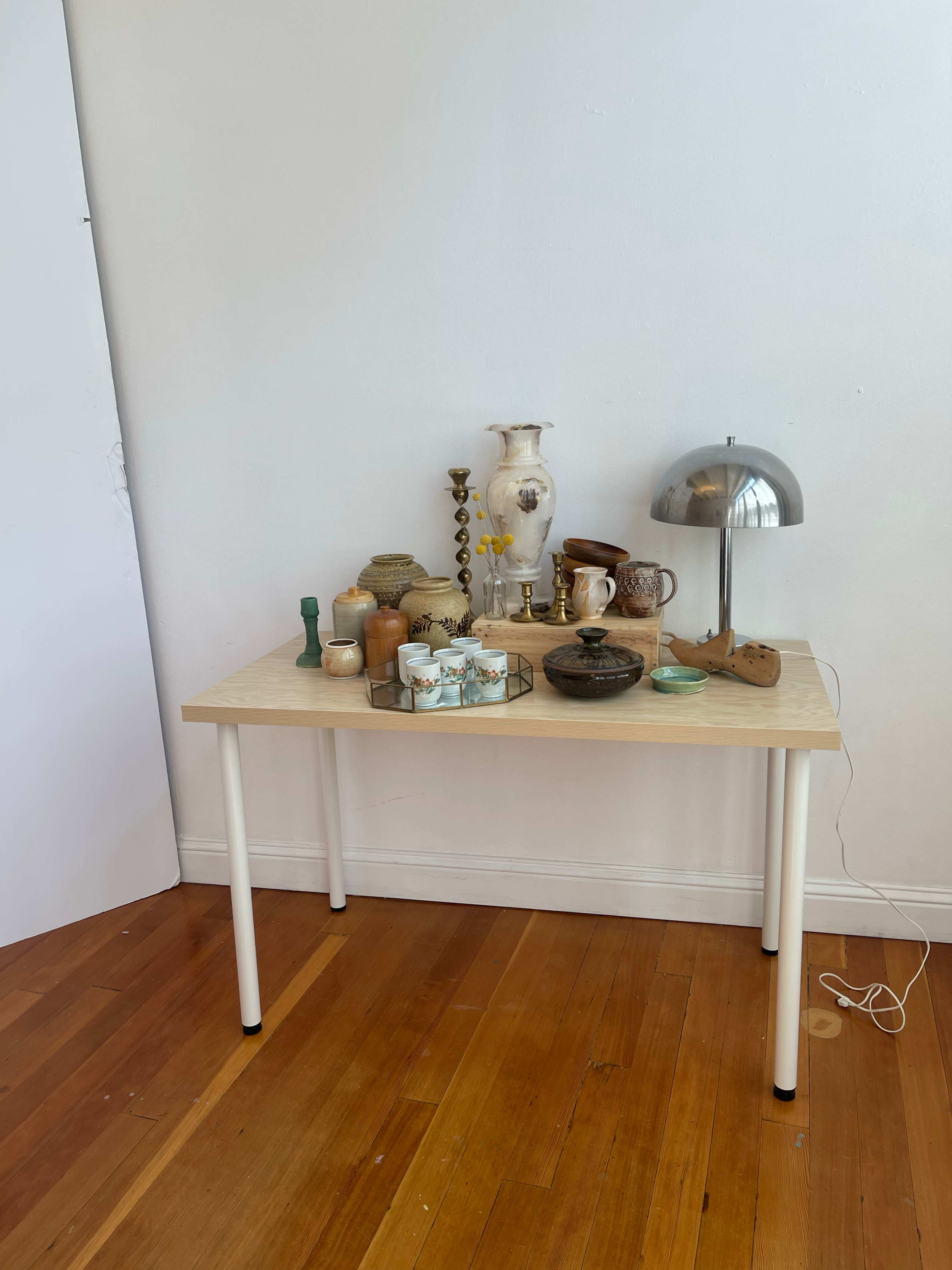 A light-colored table displays a variety of decorative items, including vases, candles, and a lamp, against a plain white wall.