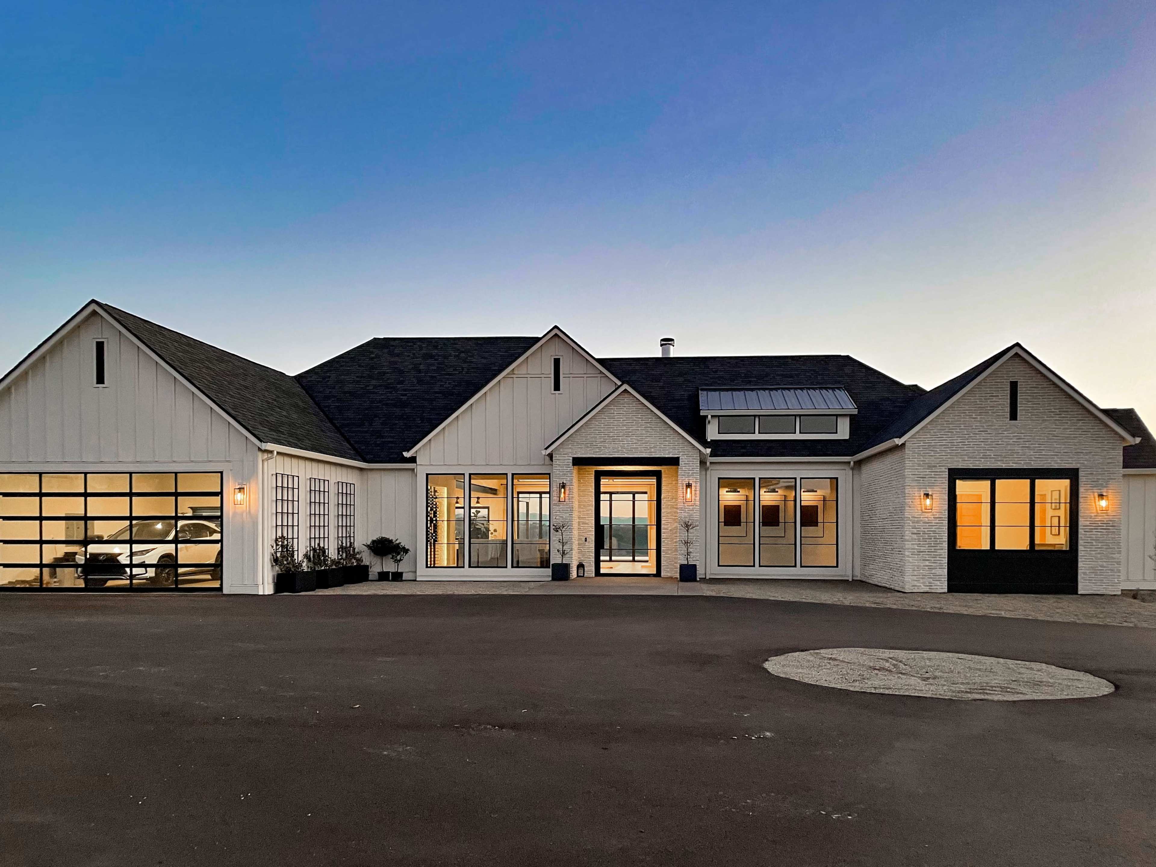 A modern single-story house features a combination of white siding and stone, with large windows and a three-car garage.