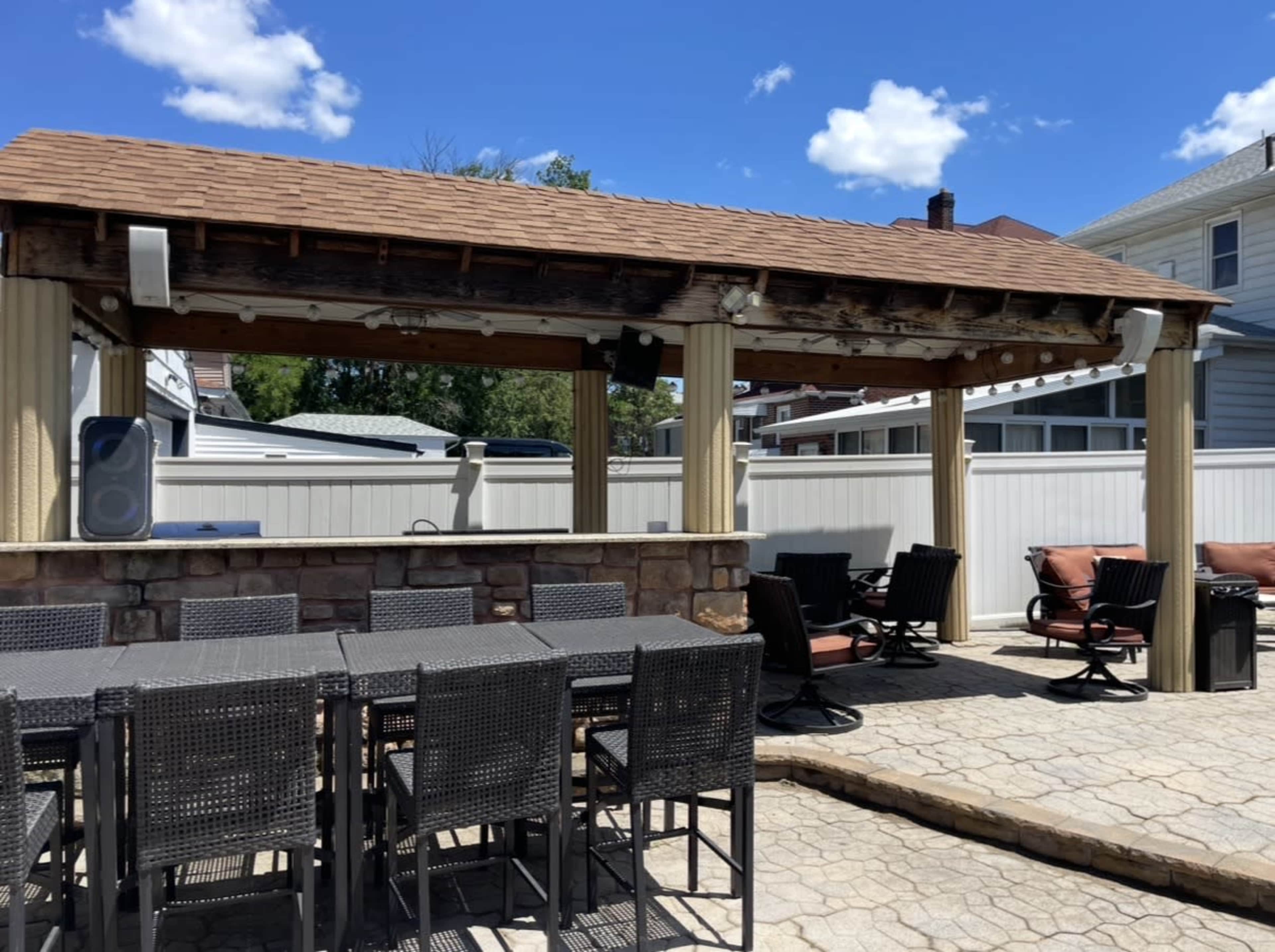 The image shows a covered outdoor patio with a stone bar and several tables and chairs arranged beneath it.