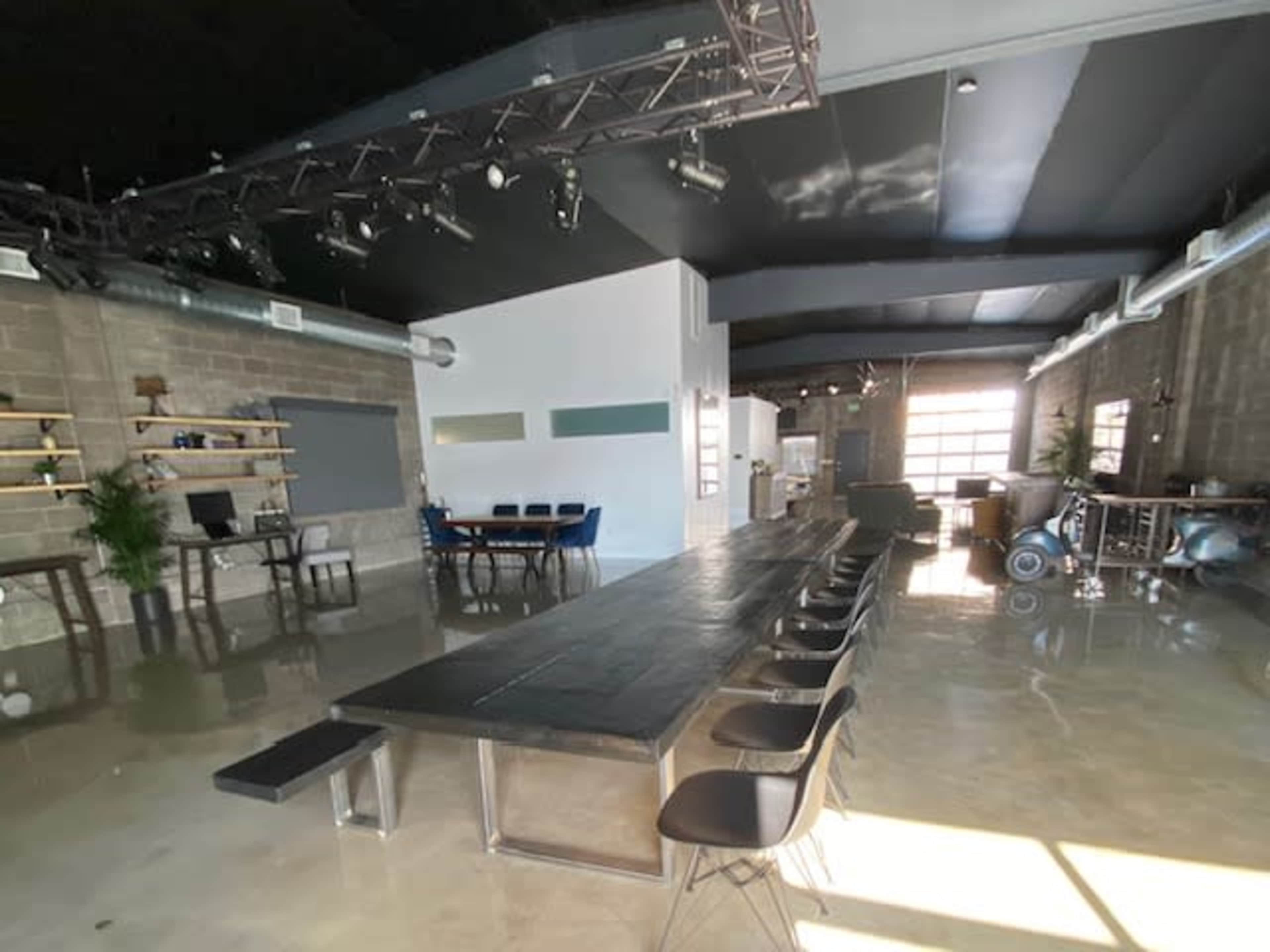 The image shows a spacious and modern meeting room with a long black table, chairs, and large windows, complemented by minimalistic decor and industrial-style walls.