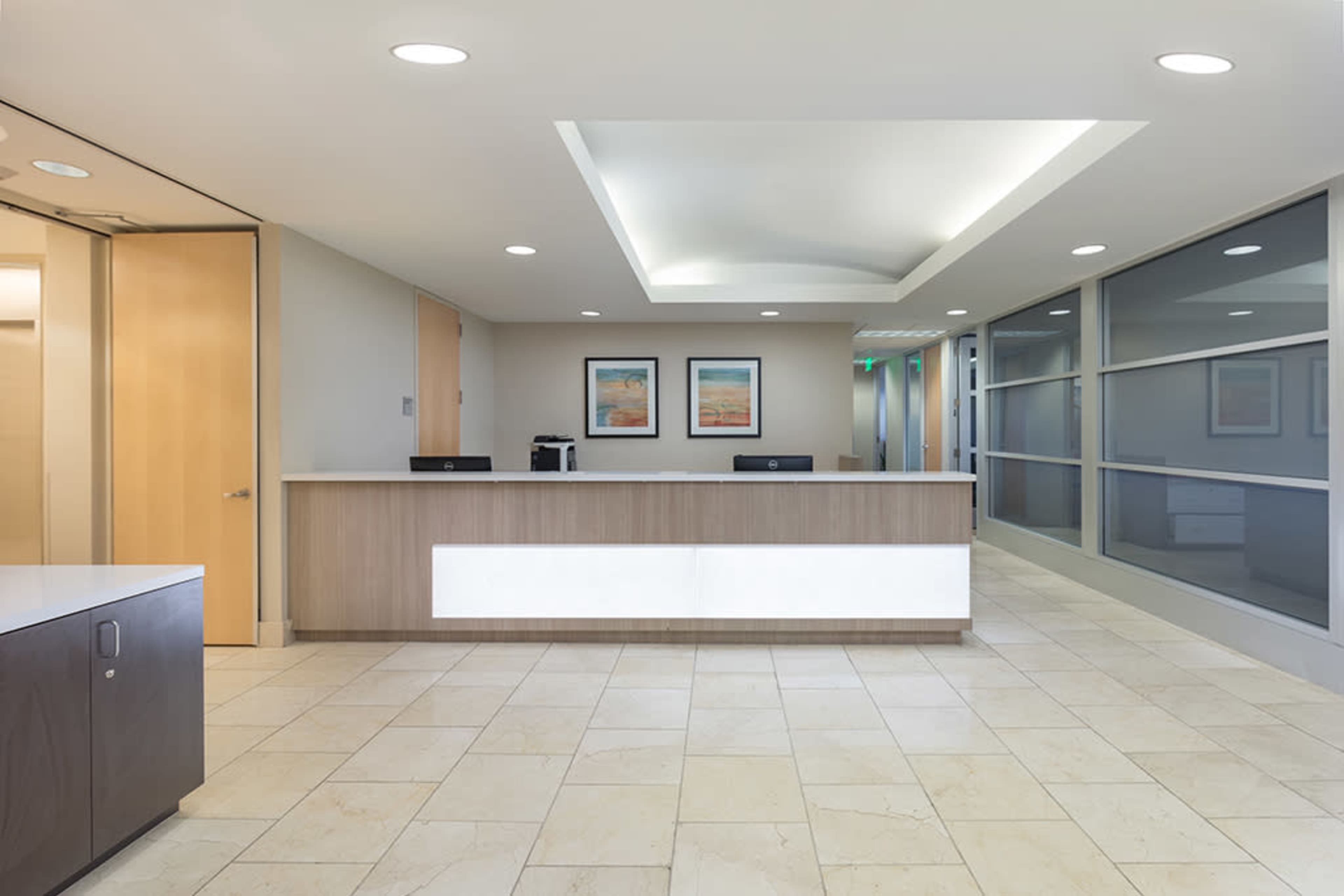A modern reception area with a sleek front desk, framed artwork on the walls, and large windows that allow natural light to enter.