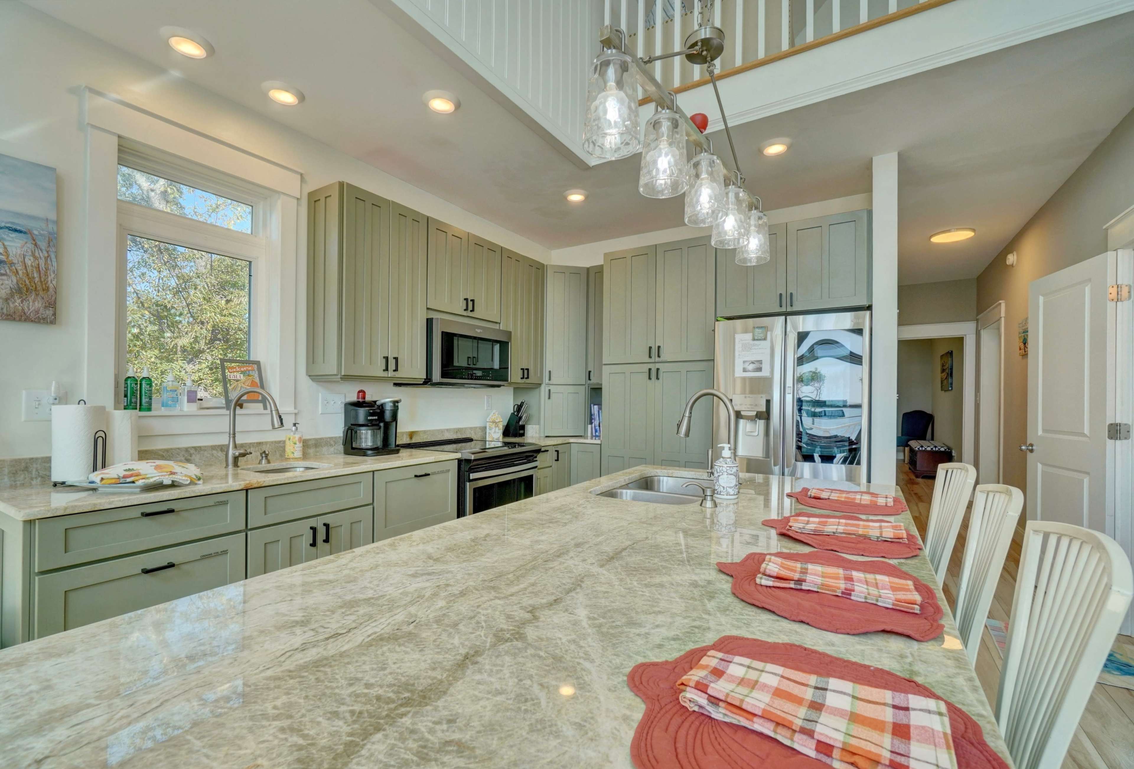 The image shows a modern kitchen with light green cabinetry, a large marble island, and pendant lighting.
