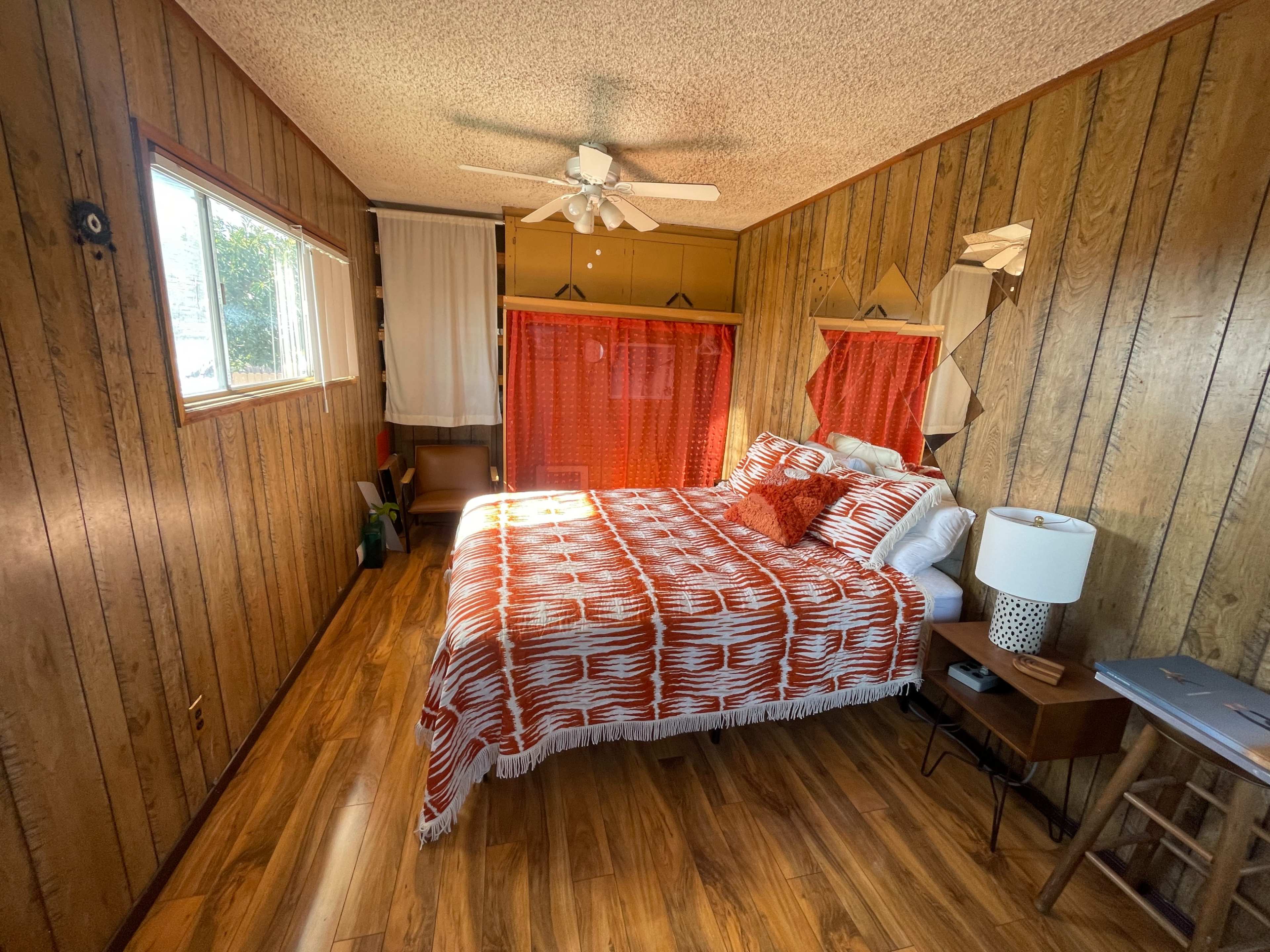 A bedroom with wooden paneling, a large bed covered with an orange and white patterned blanket, and a fan on the ceiling.