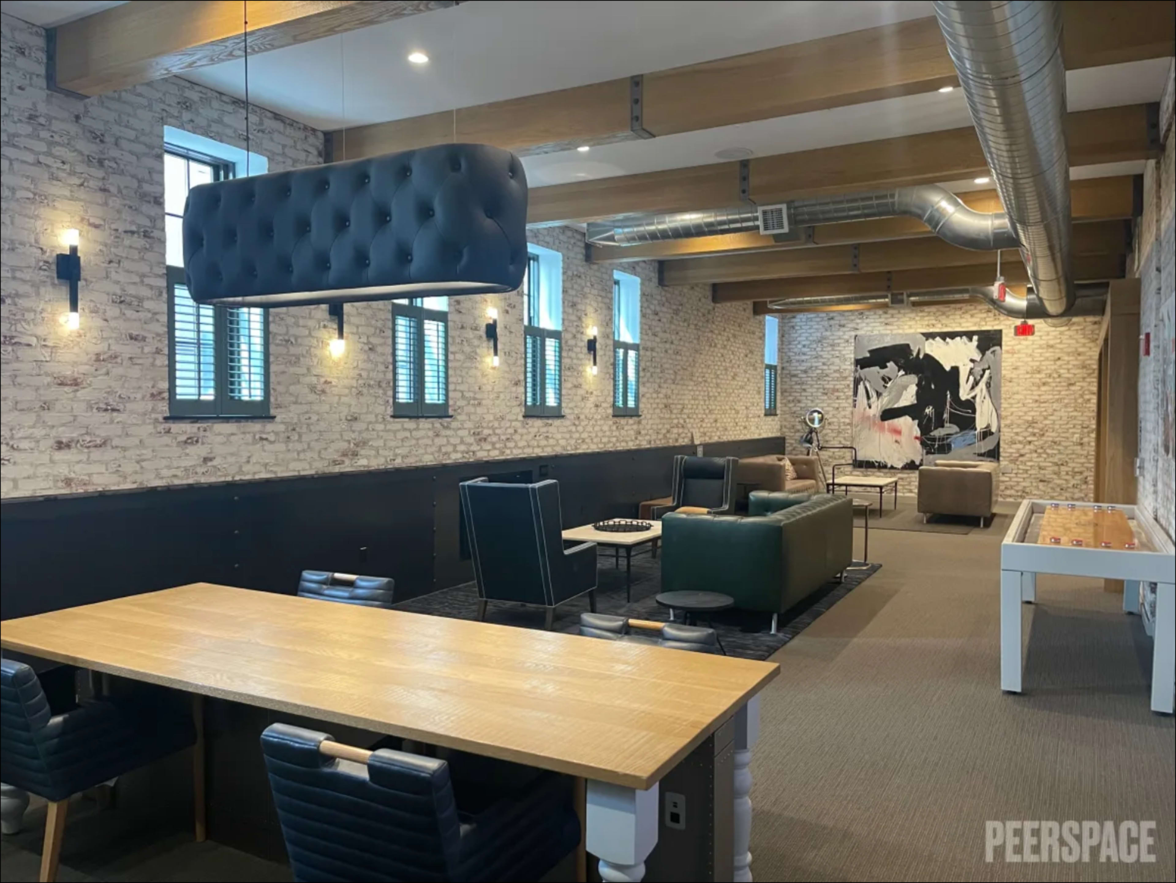 The image shows a spacious, modern lounge area with exposed brick walls, a pool table, and seating arrangements that include couches and chairs.