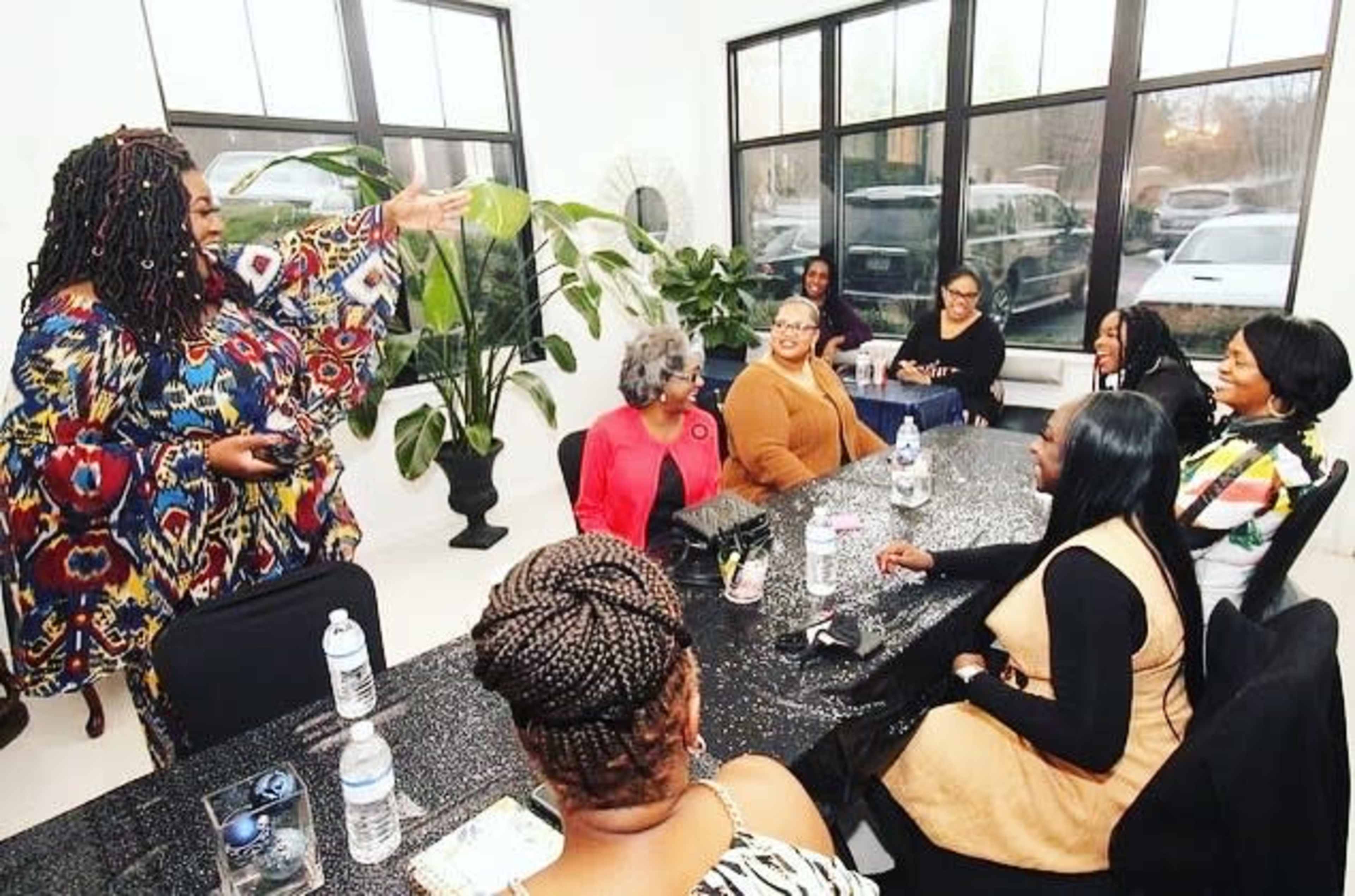 A group of women is gathered around a table in a brightly lit room, engaged in conversation and laughter.