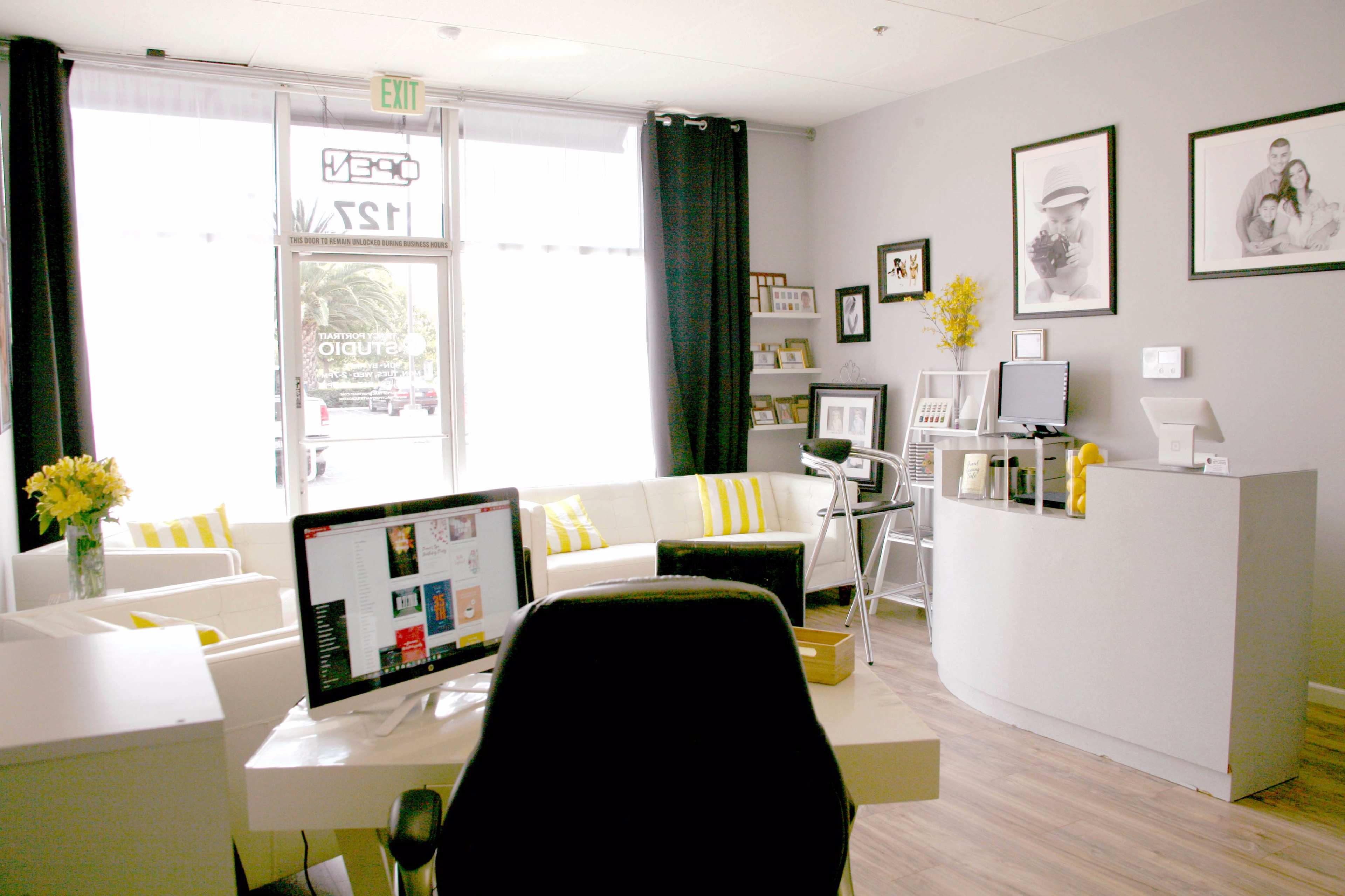 A modern studio interior with a reception desk, a computer setup, white furniture, and decorative yellow flowers.