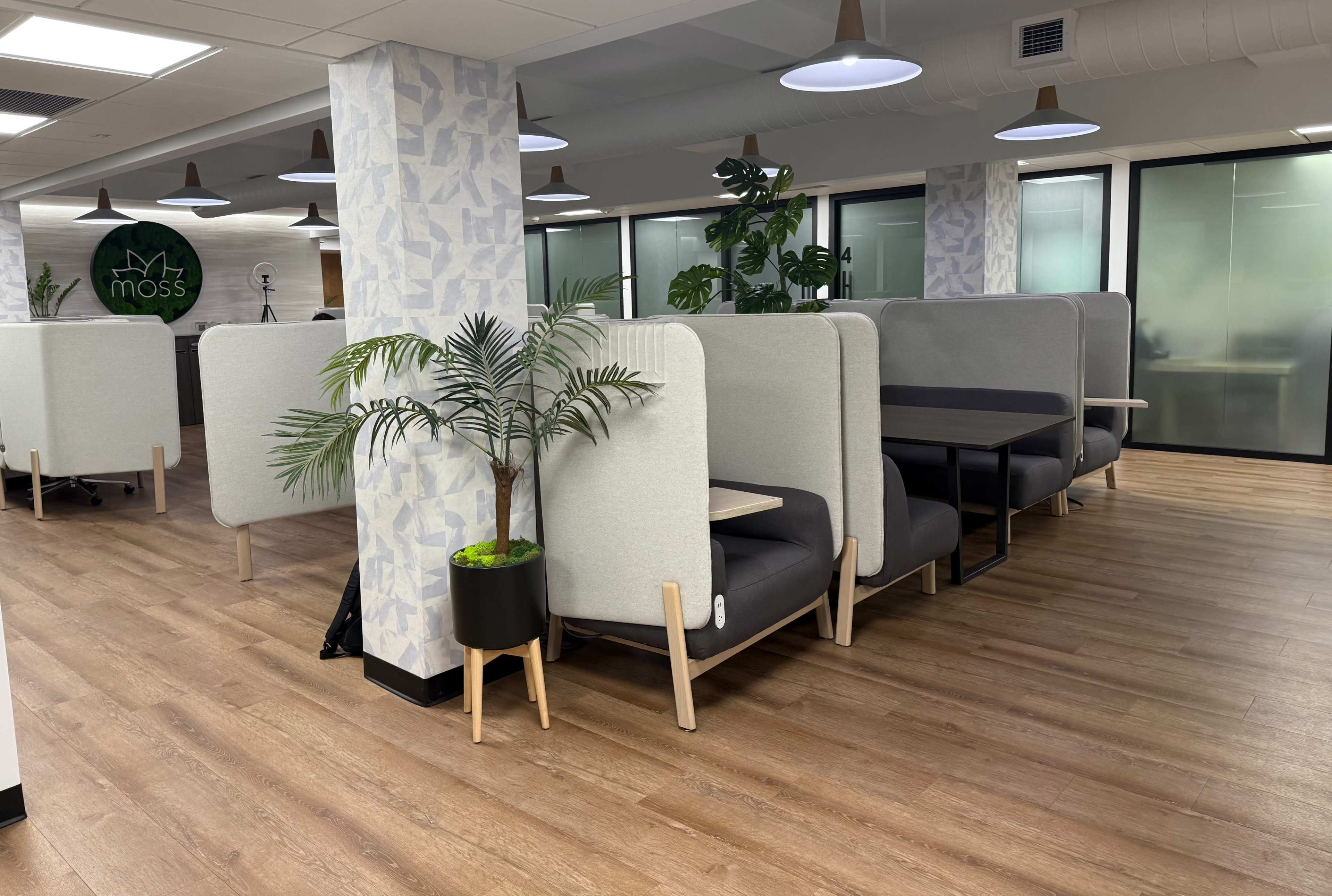 The image shows a modern office space featuring semi-private seating areas with gray fabric dividers and wooden floors.
