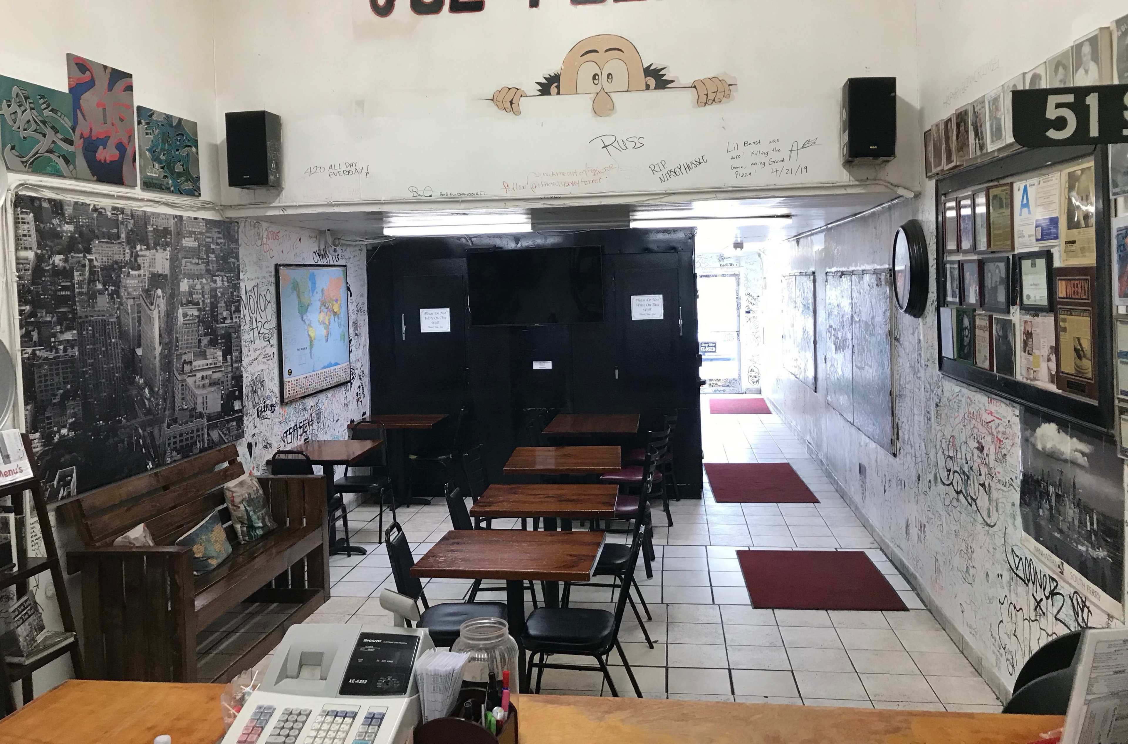 The image shows a small, partially decorated café with wooden tables, black chairs, and walls covered in graffiti.