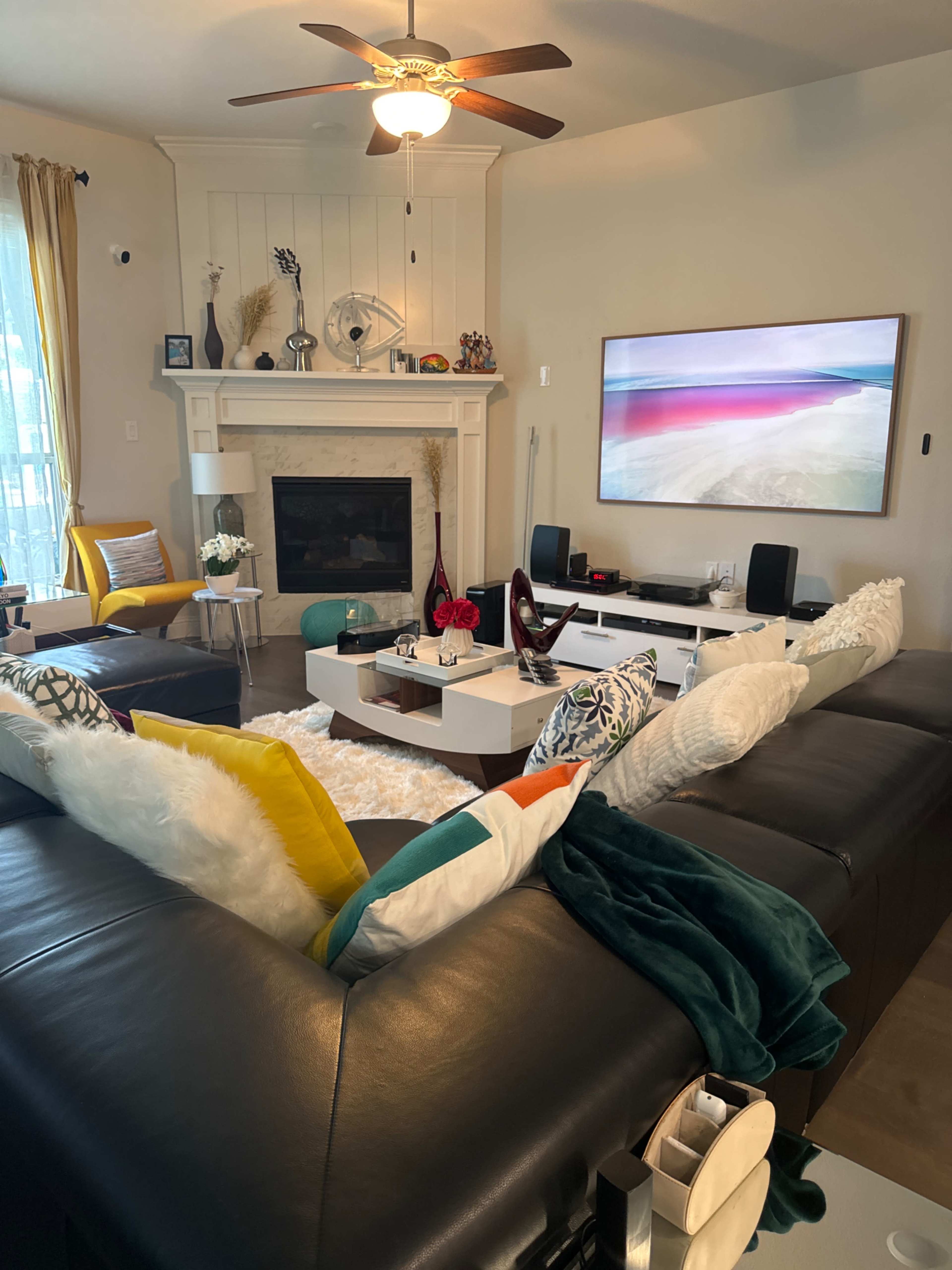A modern living room featuring a sectional sofa, a coffee table, a fireplace, and a large TV mounted on the wall.