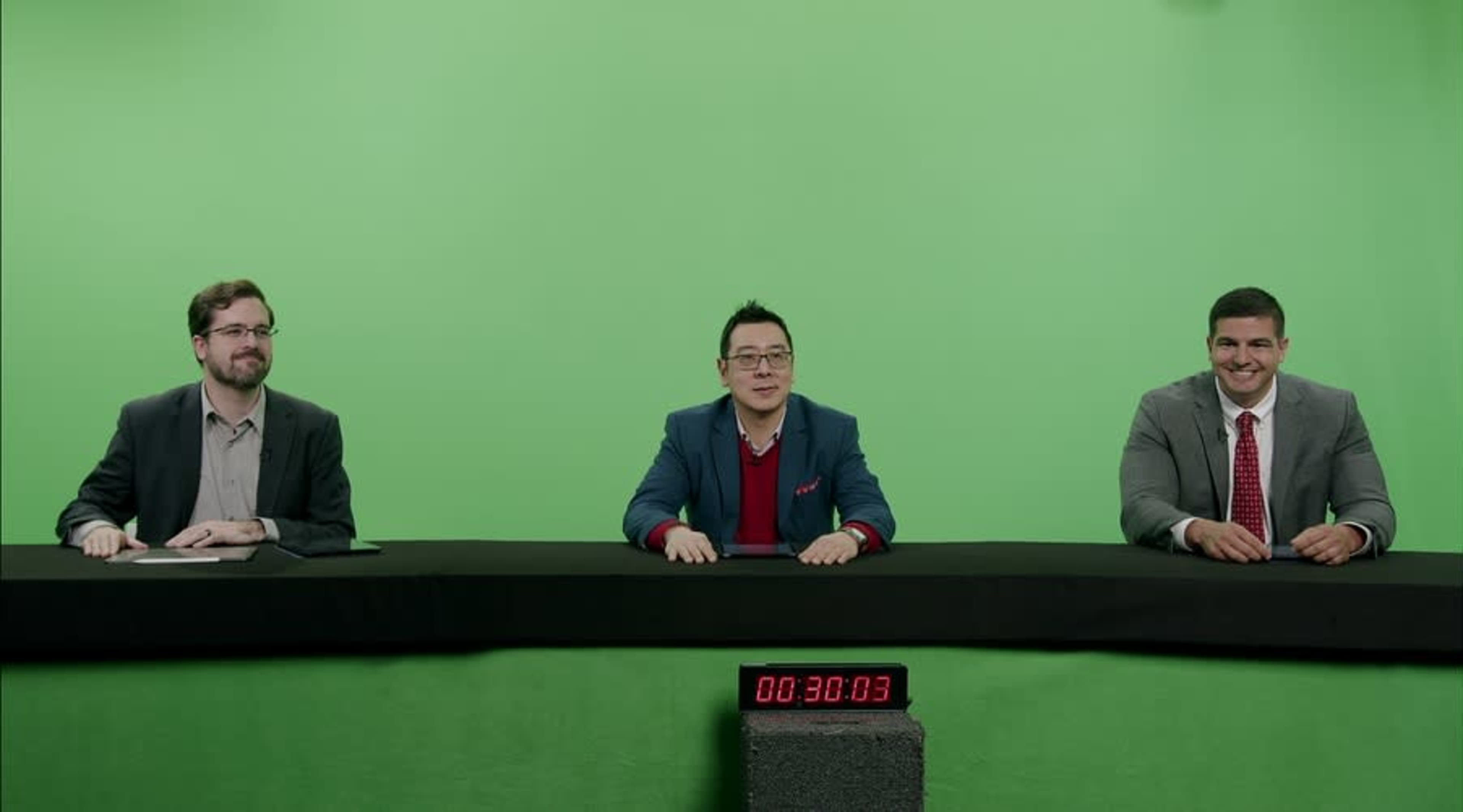 Three men sit at a long table in front of a green screen, with a digital timer displaying "00:30:03" in the foreground.