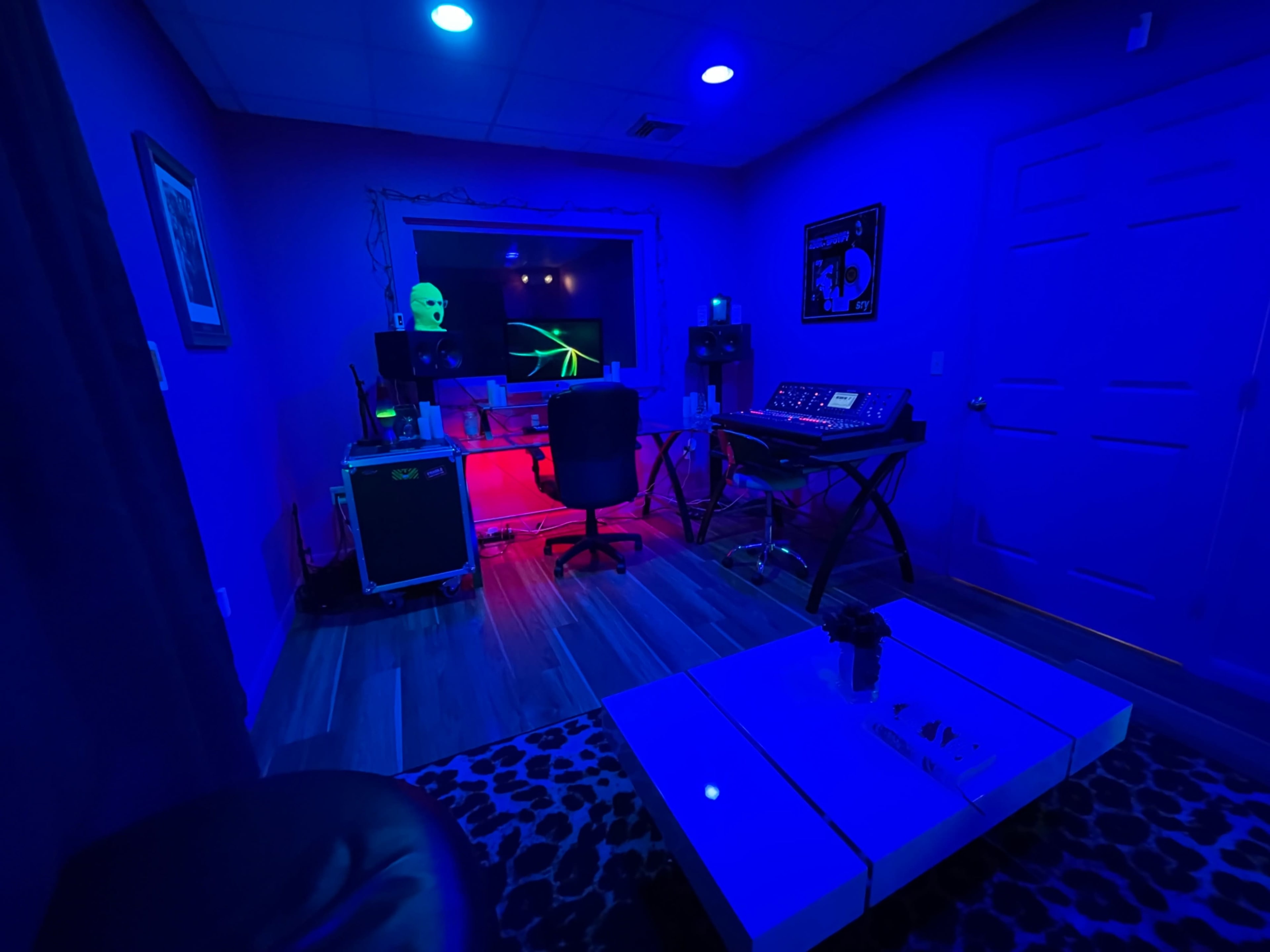 The image shows a dimly lit music studio featuring a desk with equipment, a chair, and colorful lighting effects.