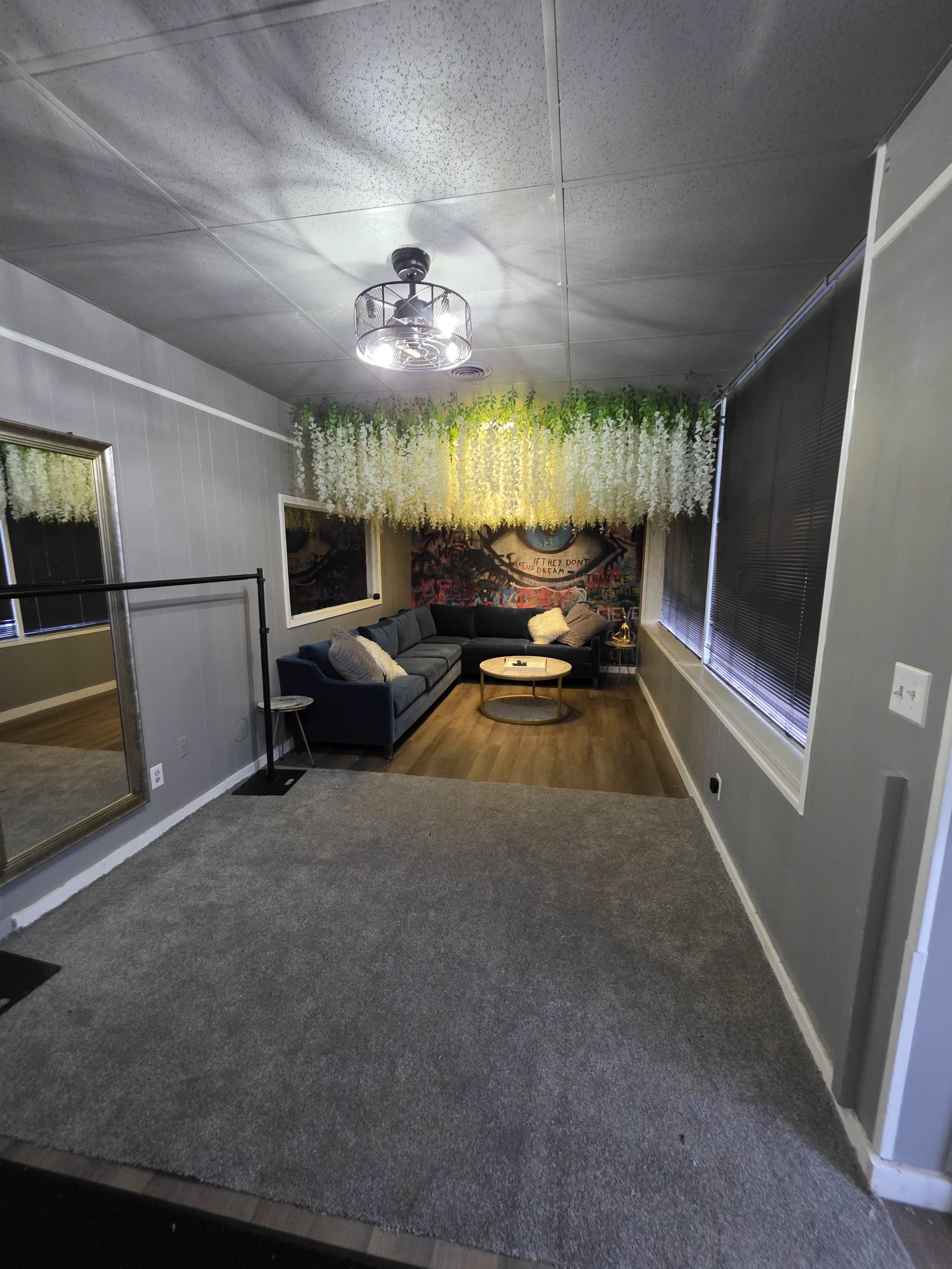The image shows a living room with a blue couch, a circular coffee table, and a wall adorned with greenery and a mural.