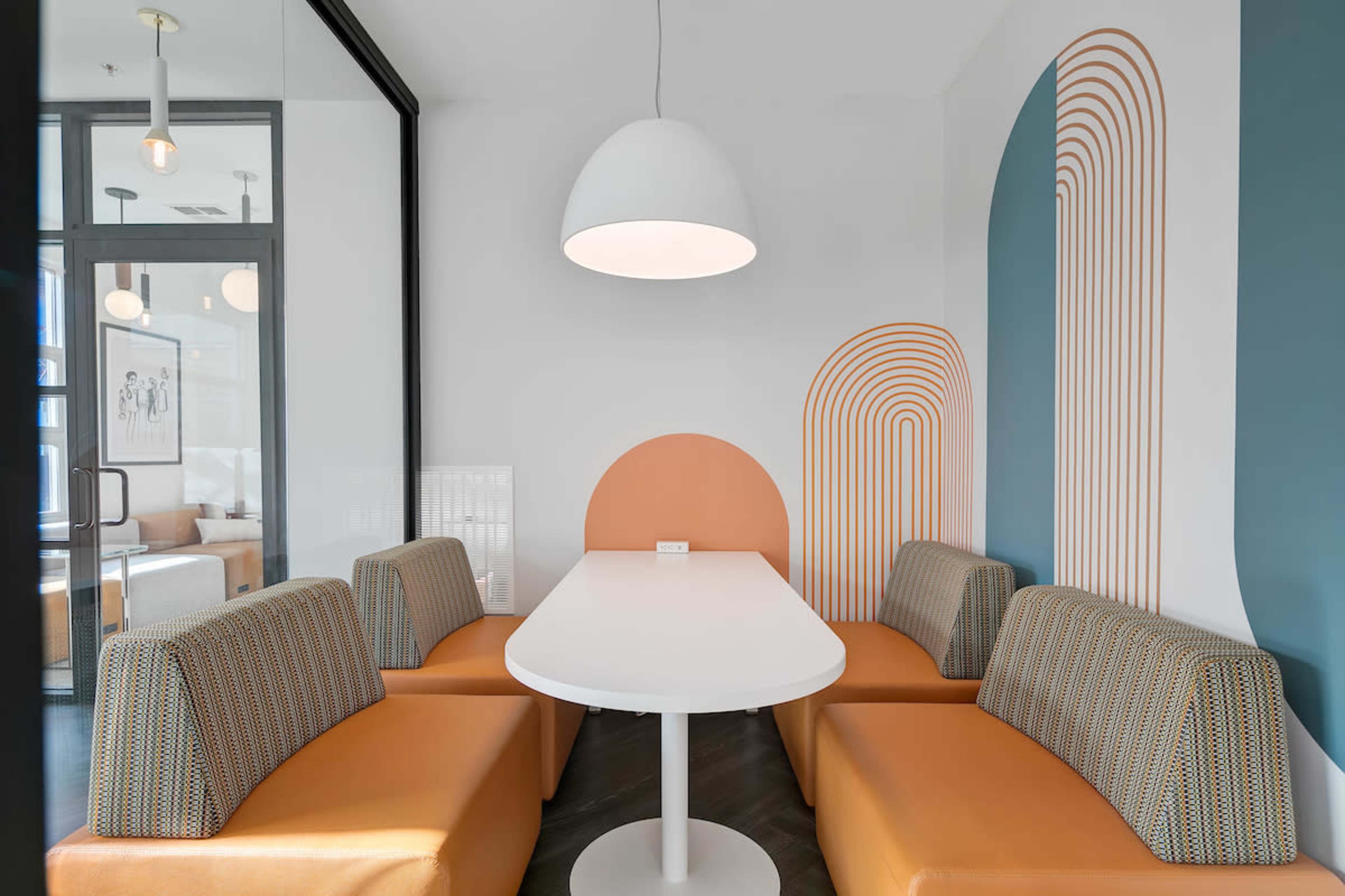 A modern seating area features a white table surrounded by orange-upholstered benches against a wall with geometric patterns.