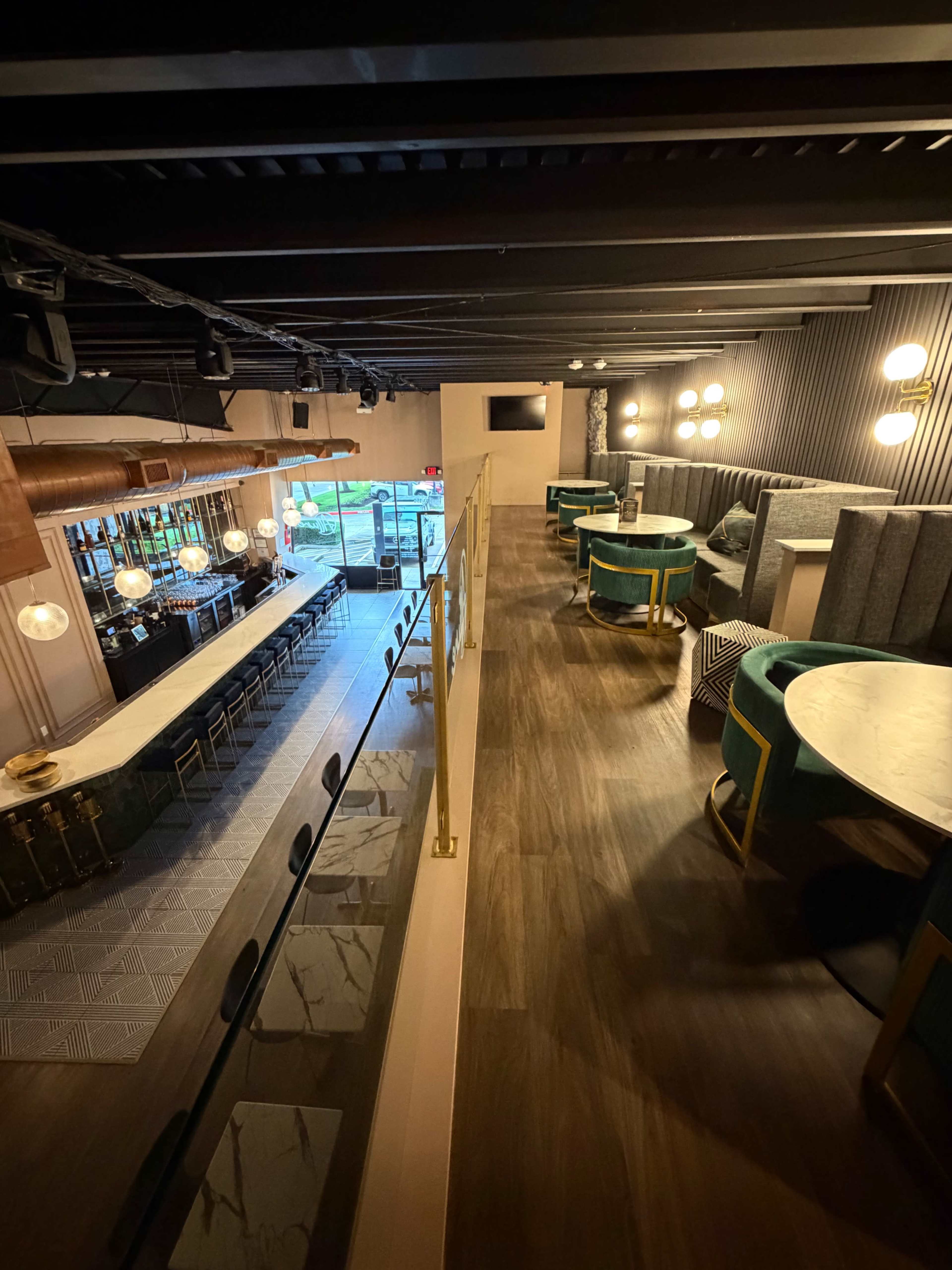 The image shows an elevated view of a modern restaurant interior featuring a bar area, seating arrangements, and large windows allowing natural light to enter.