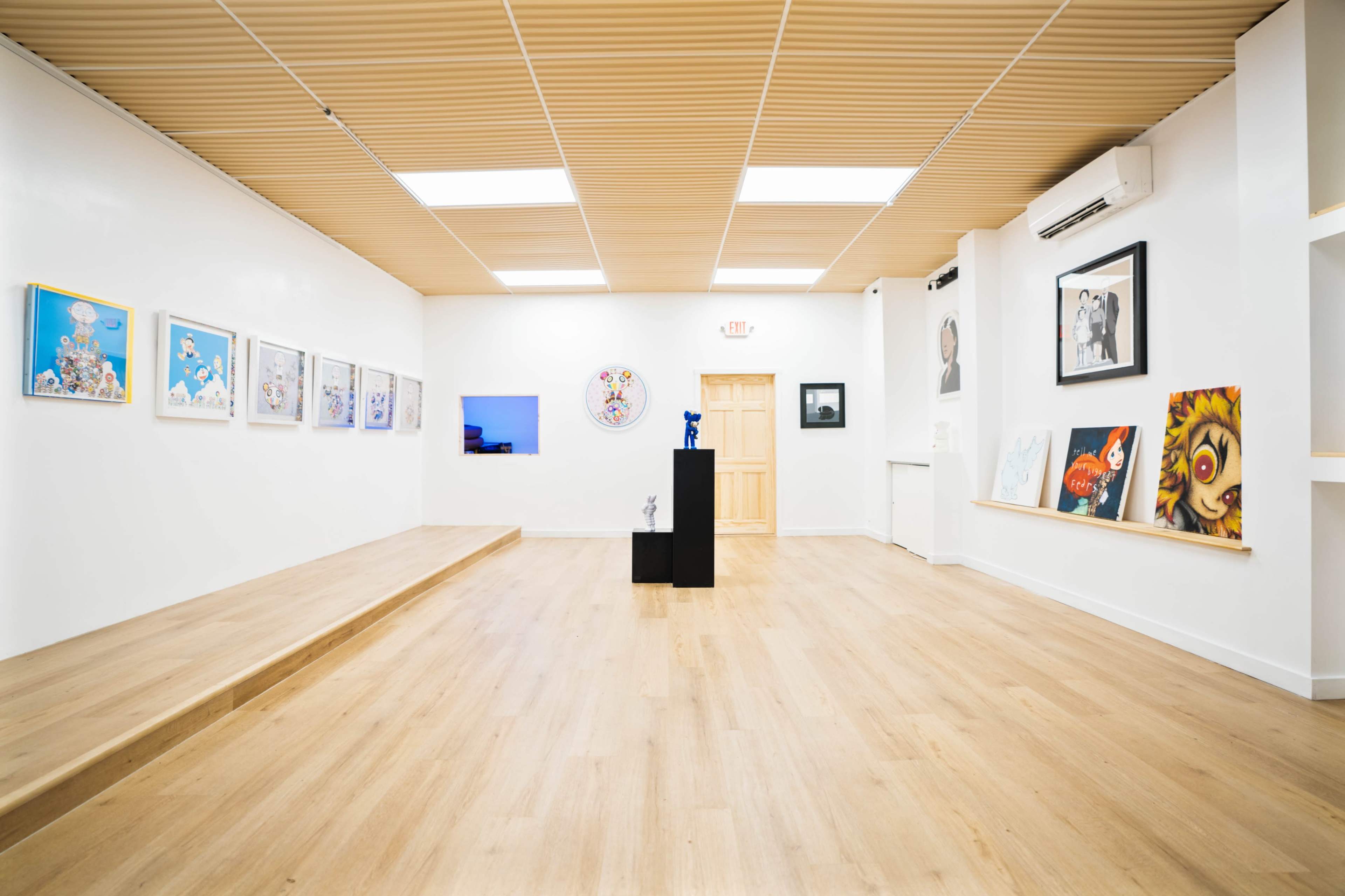 An art gallery featuring an array of framed artworks on the white walls and a central black pedestal displaying a sculpture.