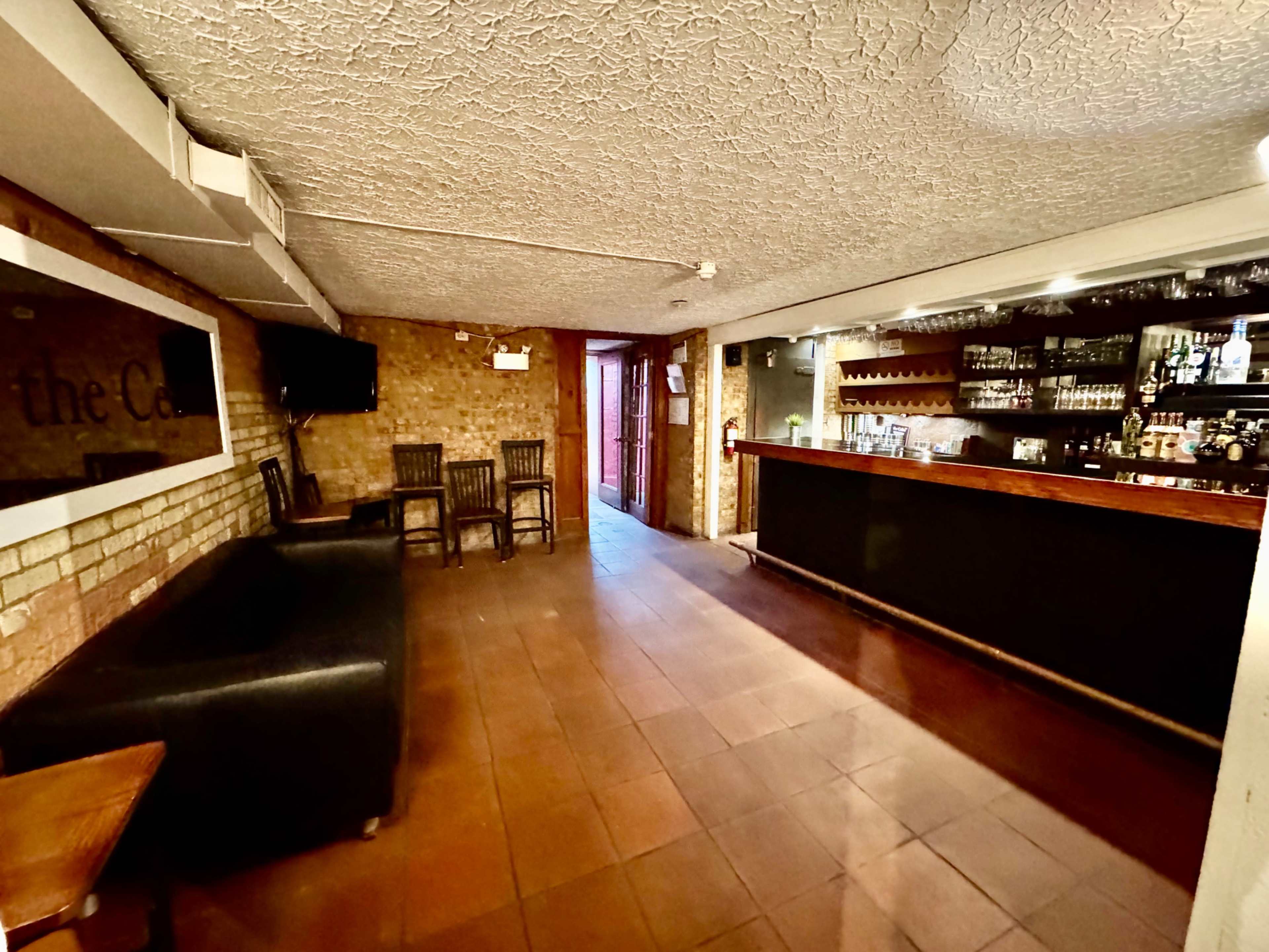 A spacious bar area with a dark countertop, several chairs, and a doorway leading outside.