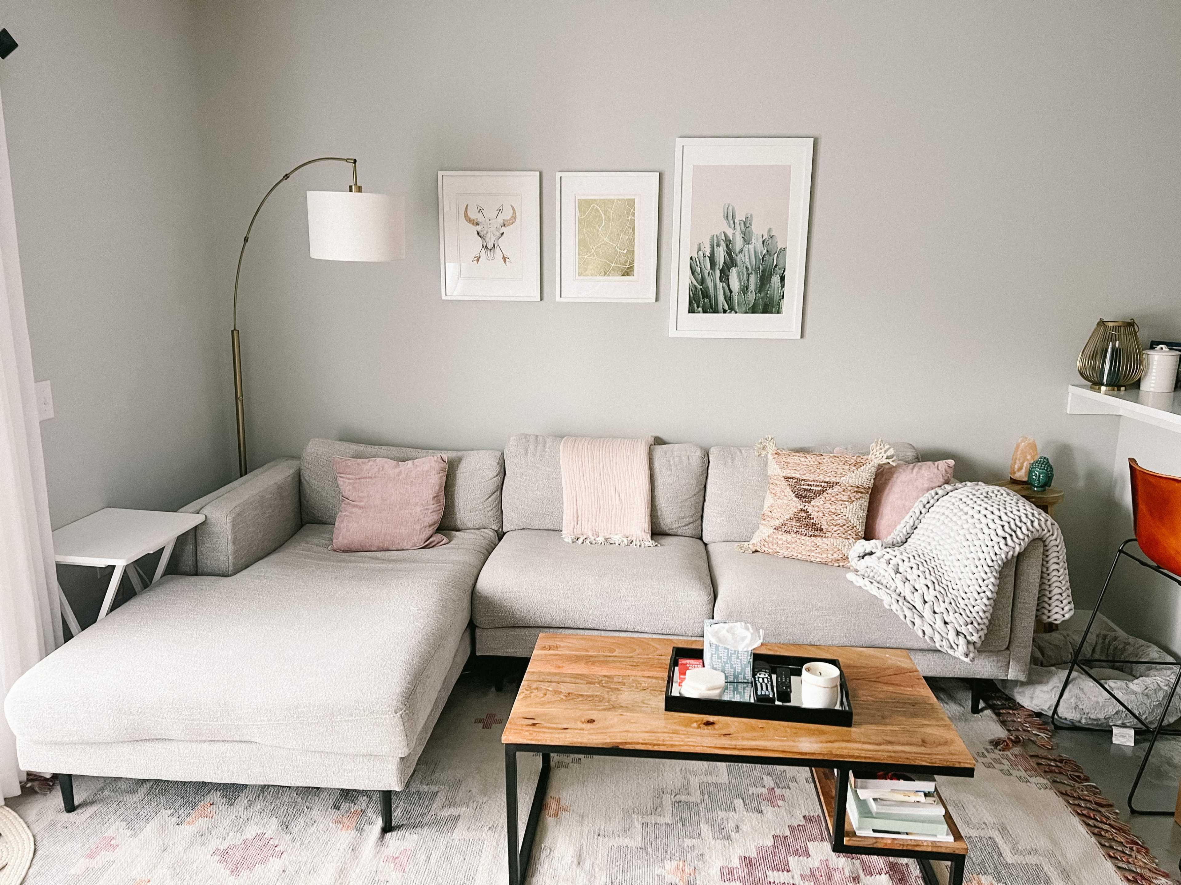 A modern living room features a gray sectional sofa with decorative pillows, a wooden coffee table, and framed artworks on the wall.