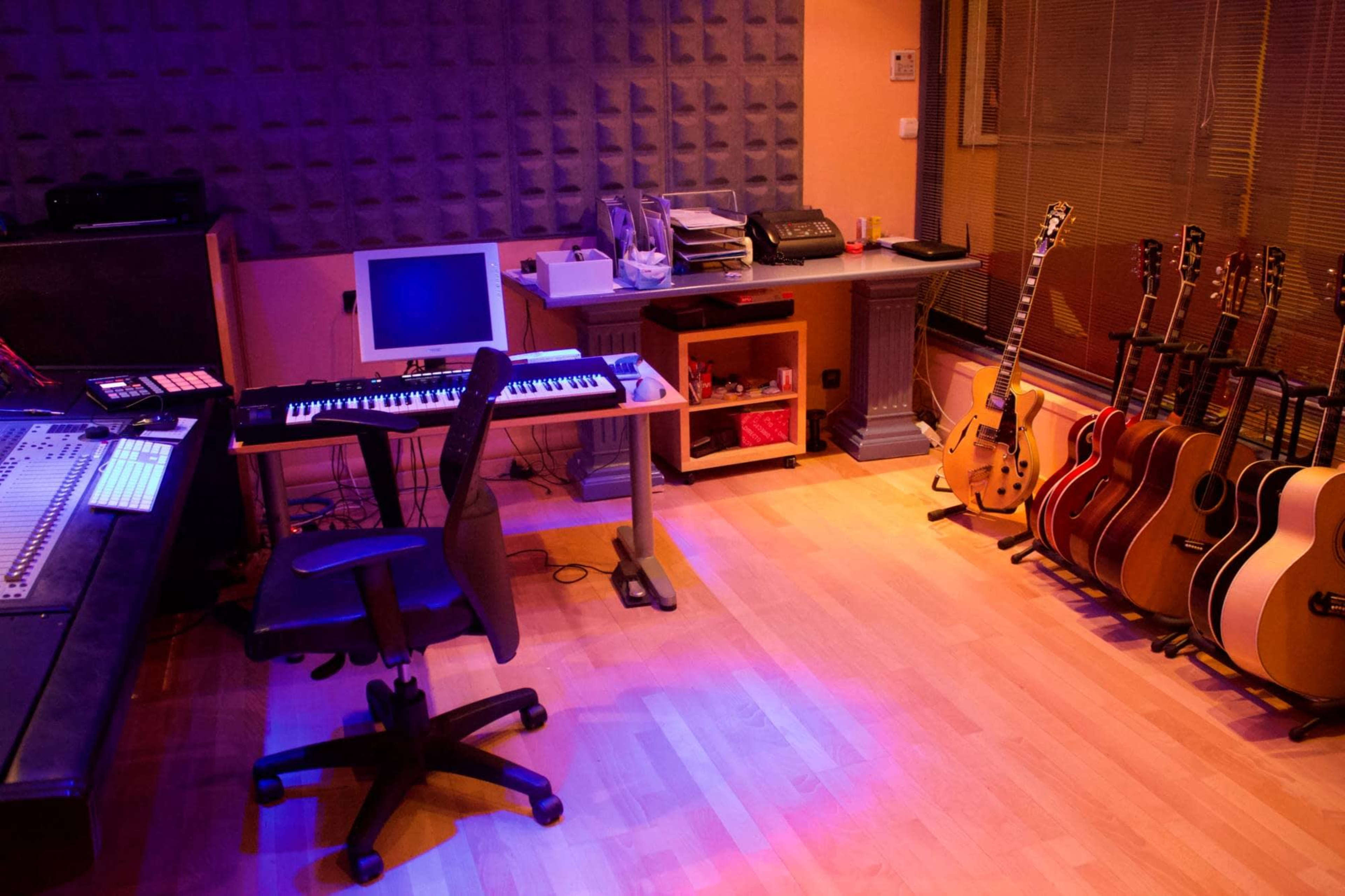 A music studio with a keyboard, computer, desk, and a row of acoustic guitars against the wall.