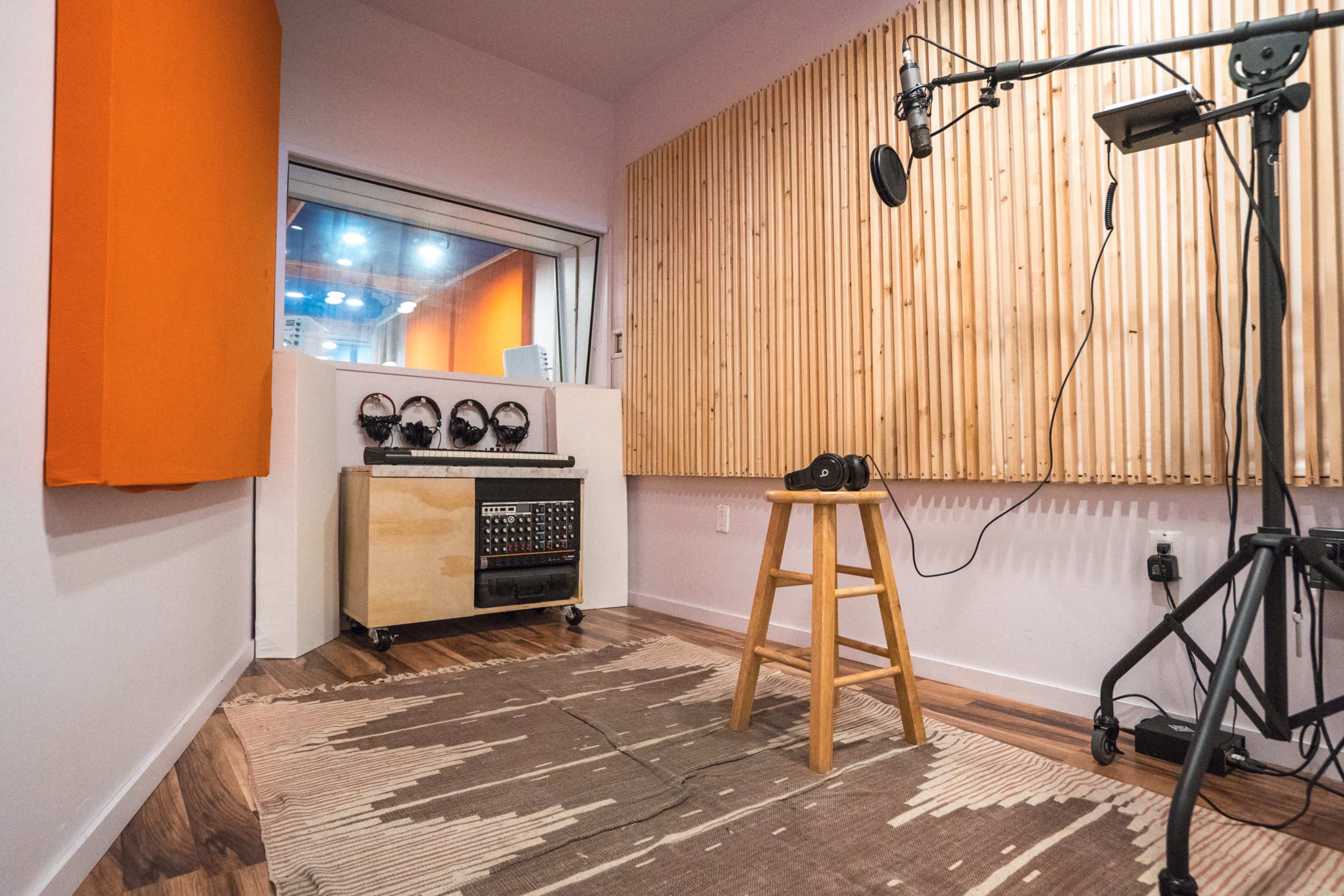 A small recording studio features acoustic panels, a microphone on a stand, a stool, and sound equipment.