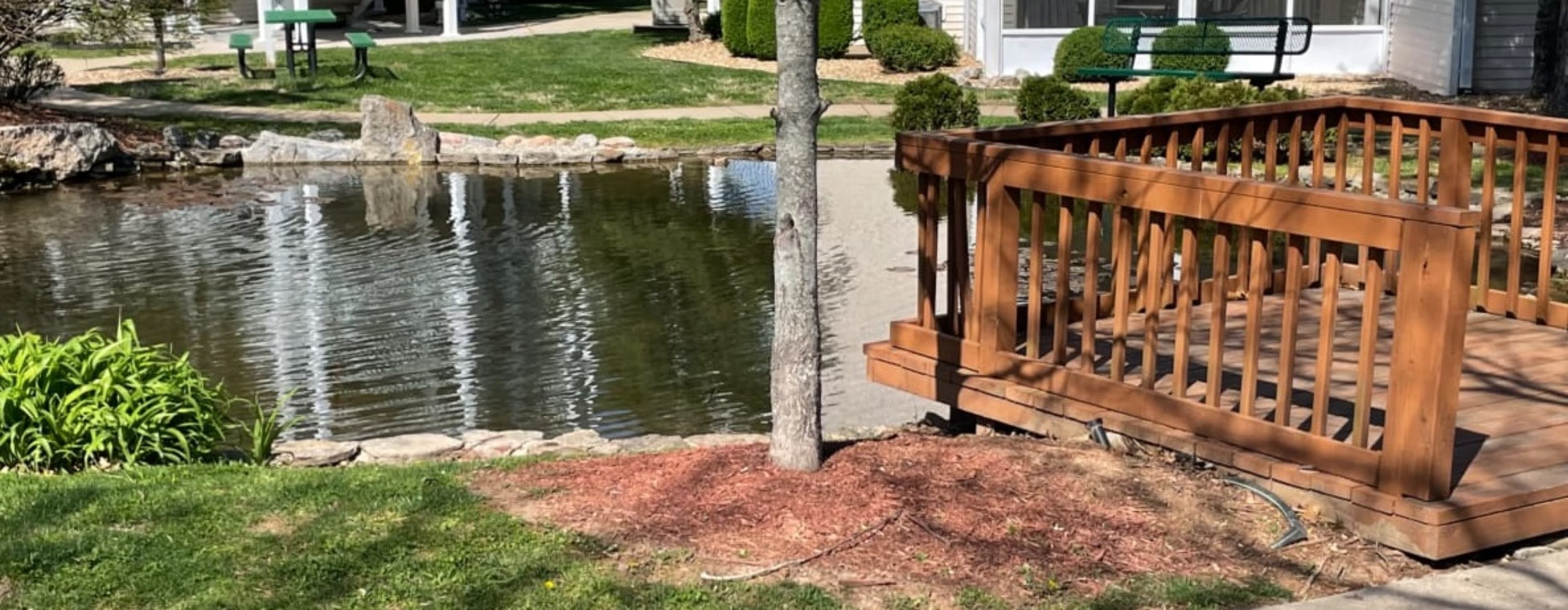A wooden deck overlooks a pond surrounded by grass and landscaping features.