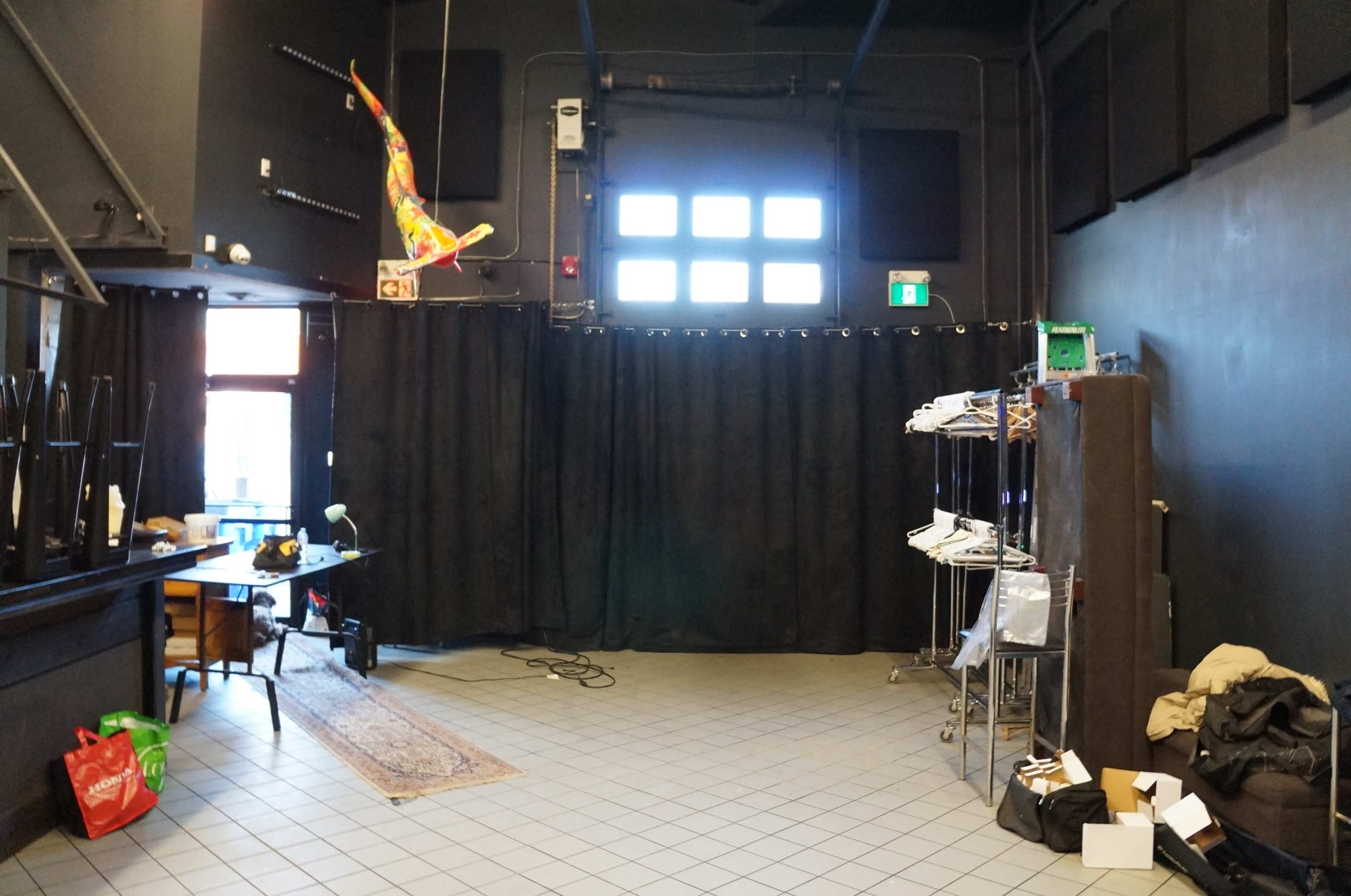 A dimly lit room features a black curtain, a table with equipment, and several clothing racks against a wall.