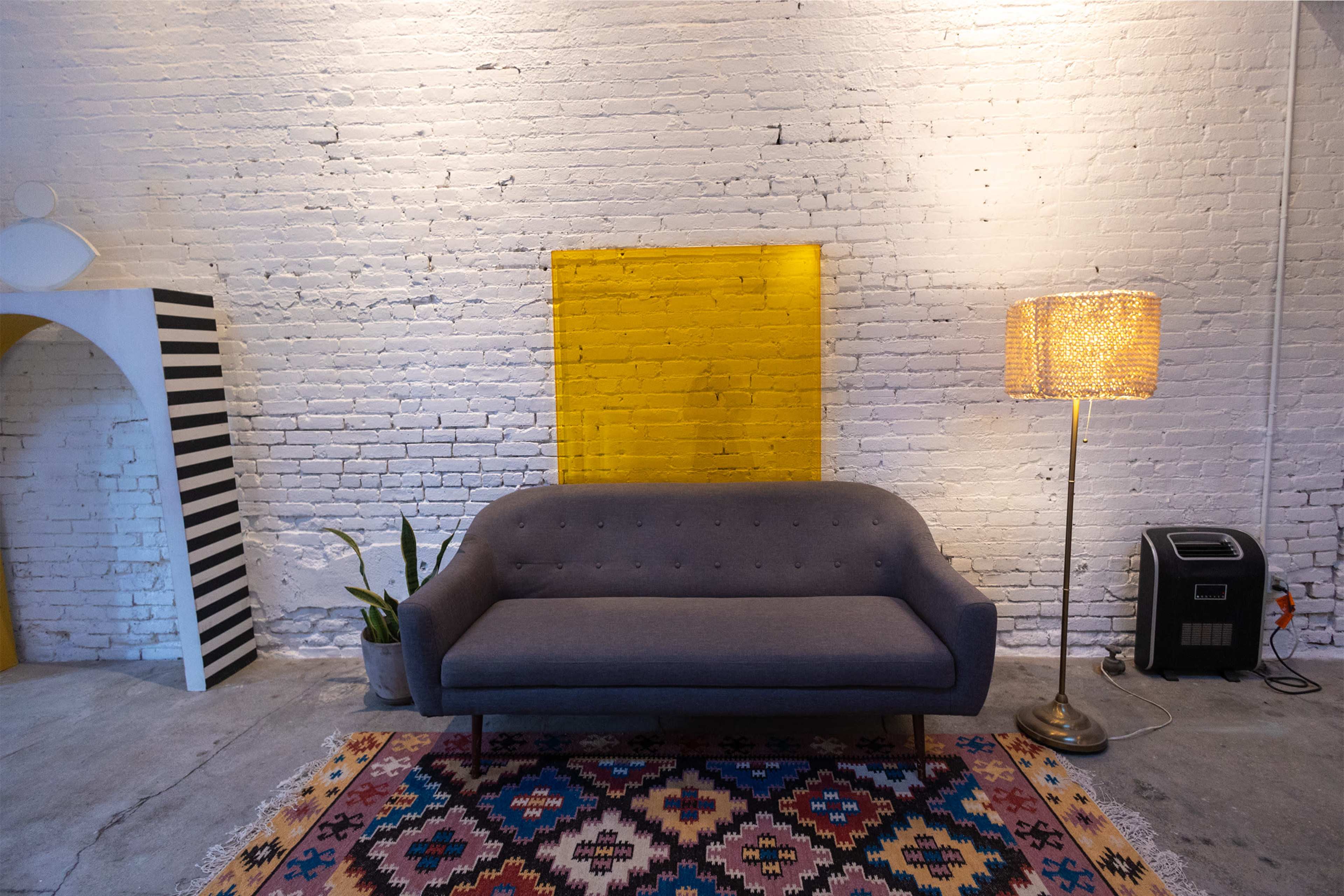 A gray sofa in front of a yellow accent wall, with a patterned rug on the floor and a lamp beside it.