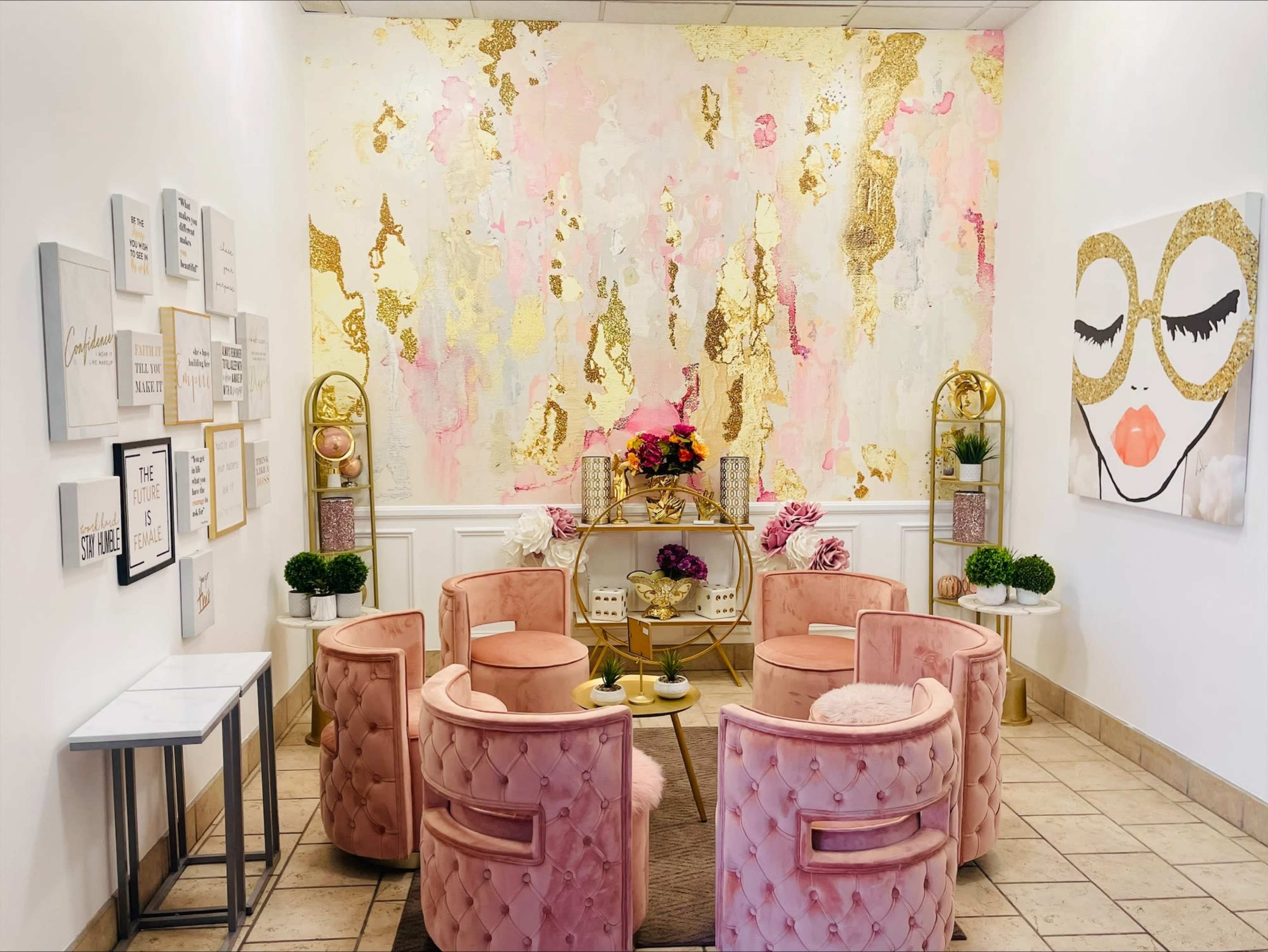 A stylish lounge area with pink upholstered chairs arranged around a central table, set against a colorful abstract wall and adorned with decorative artwork and plants.
