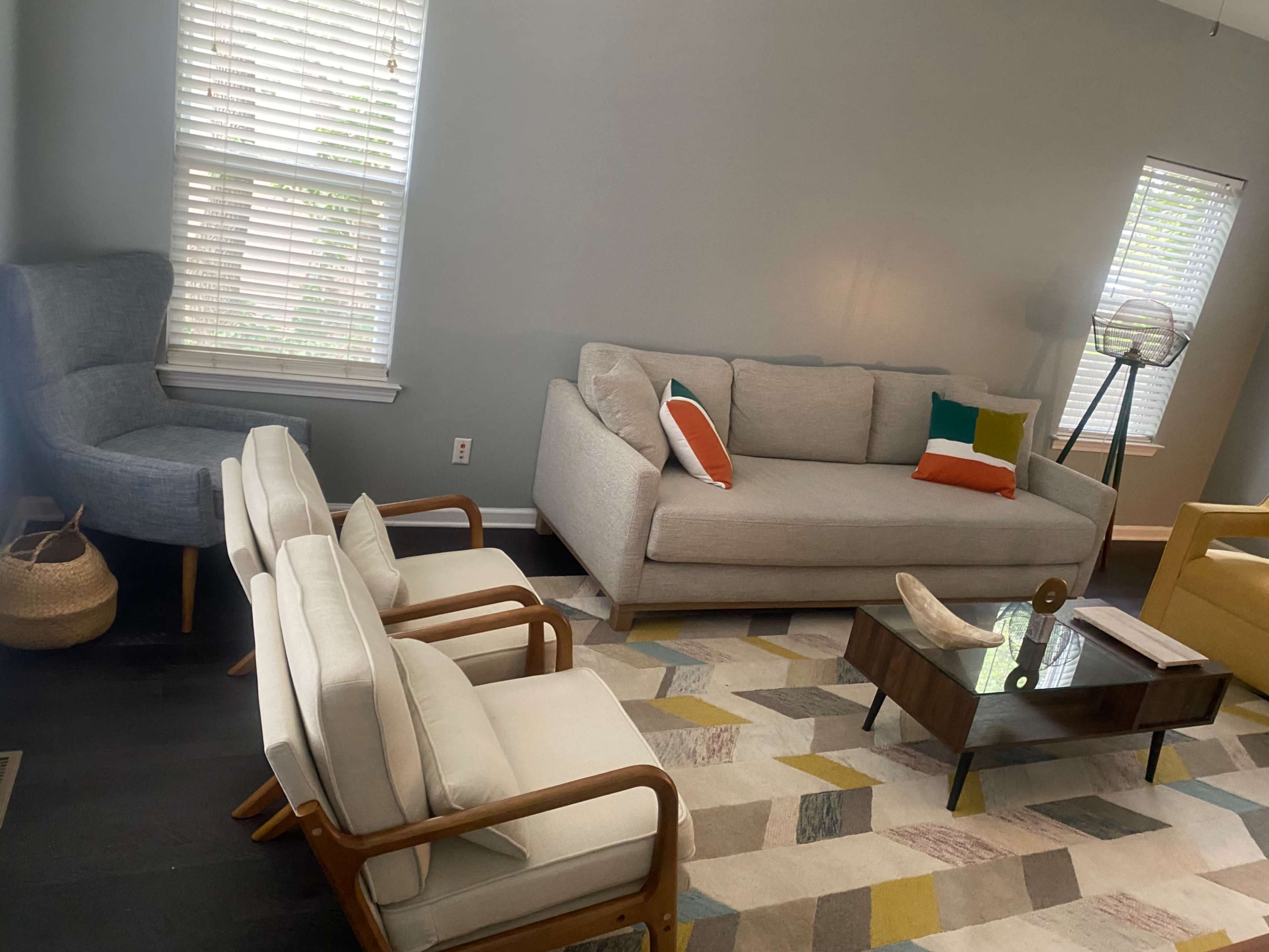The image shows a living room with a gray sofa, two white armchairs, a brown coffee table, and a colorful area rug.