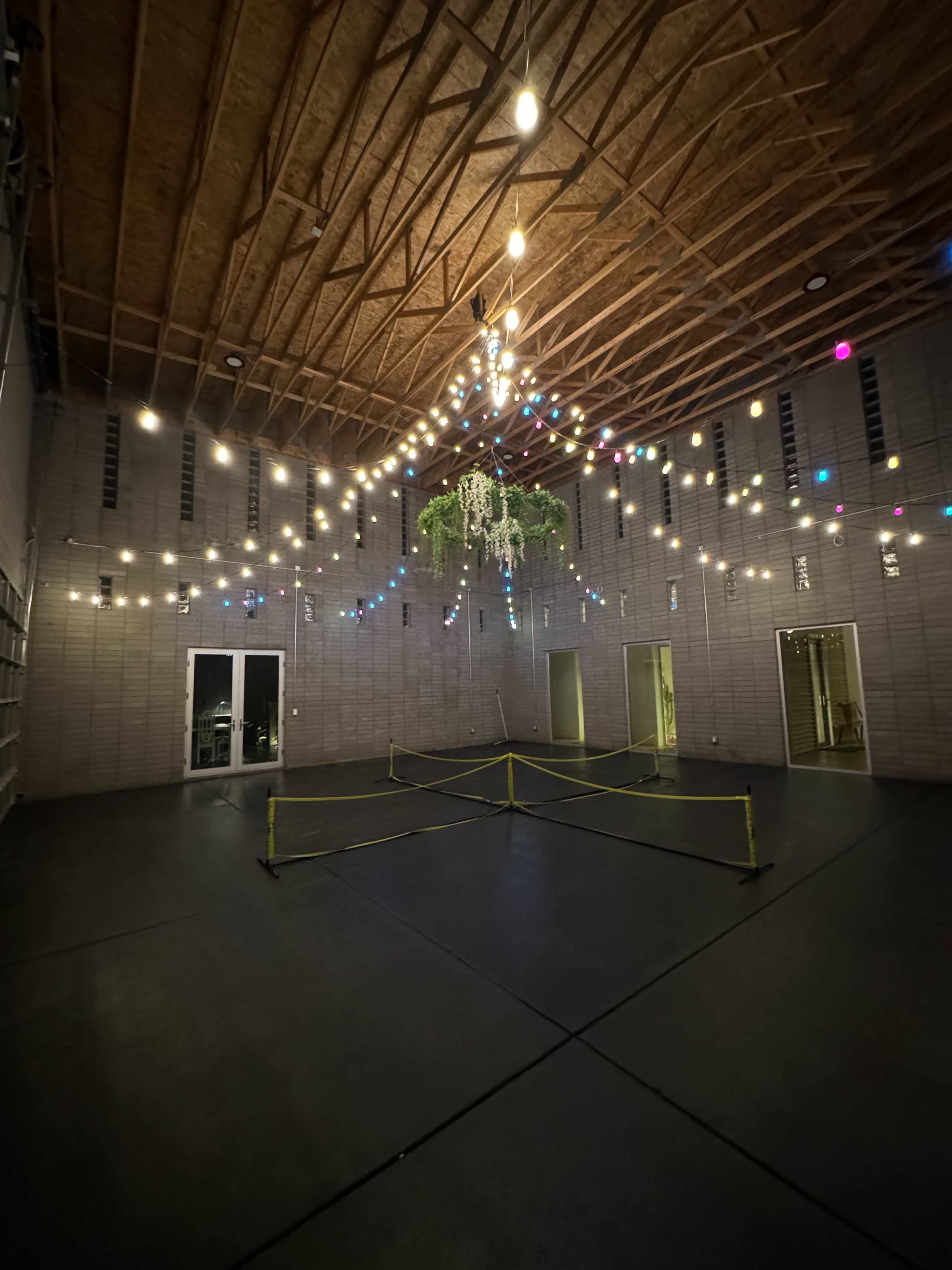 An empty room with a high wooden ceiling, decorated with string lights and a chandelier, and a sectioned-off area in the center.