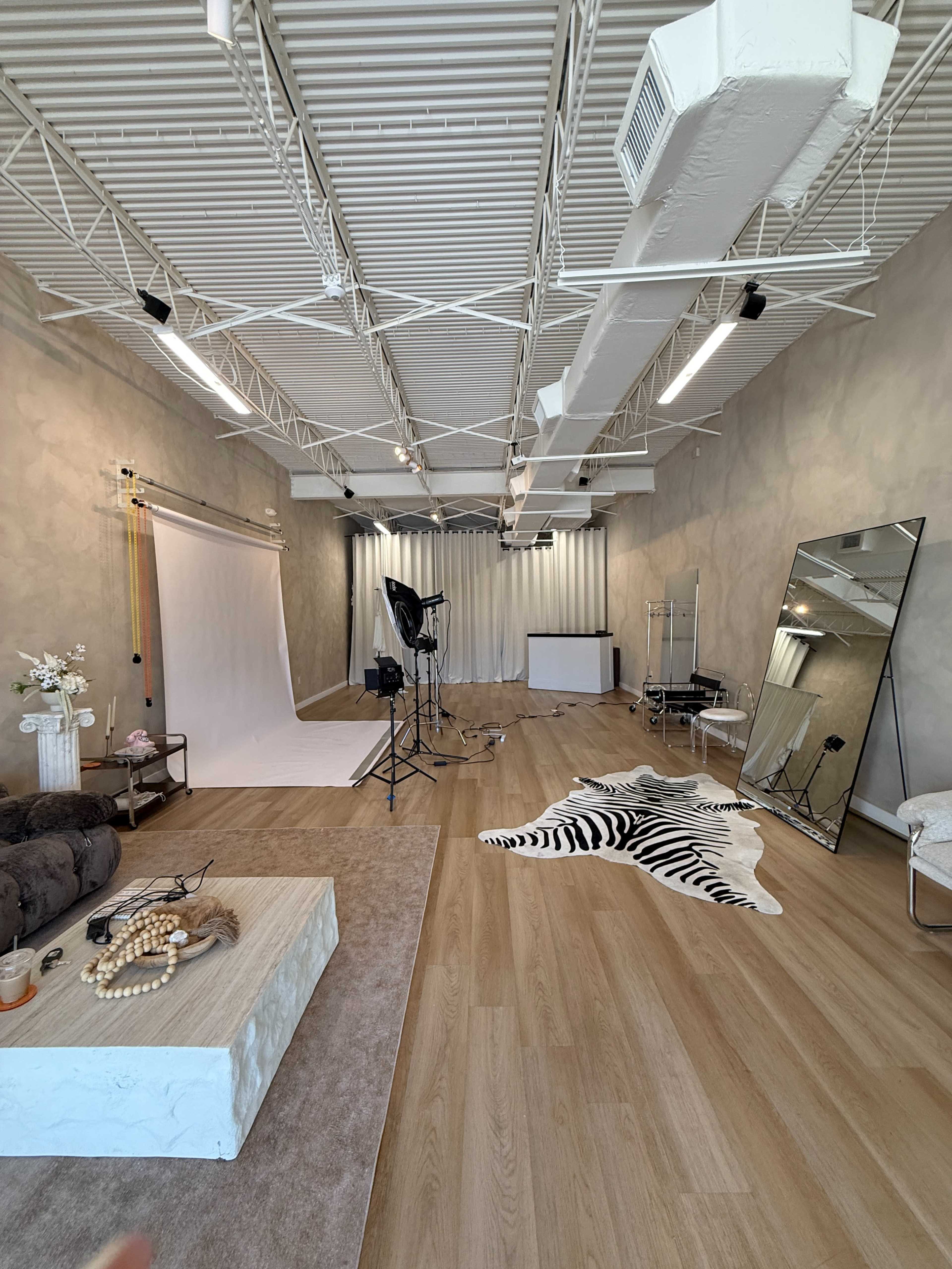 The image shows a photography studio with a white backdrop, lighting equipment, a large mirror, and various decorative elements on a wooden floor.
