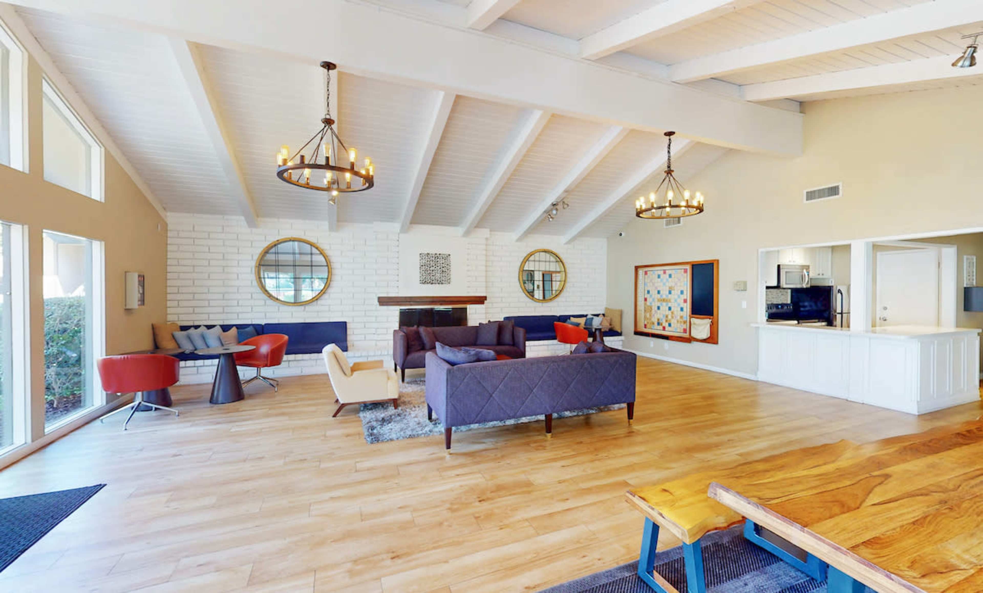 The image depicts a spacious, modern lounge area with high ceilings, featuring comfortable seating arrangements, a large wooden table, and large windows allowing ample natural light.