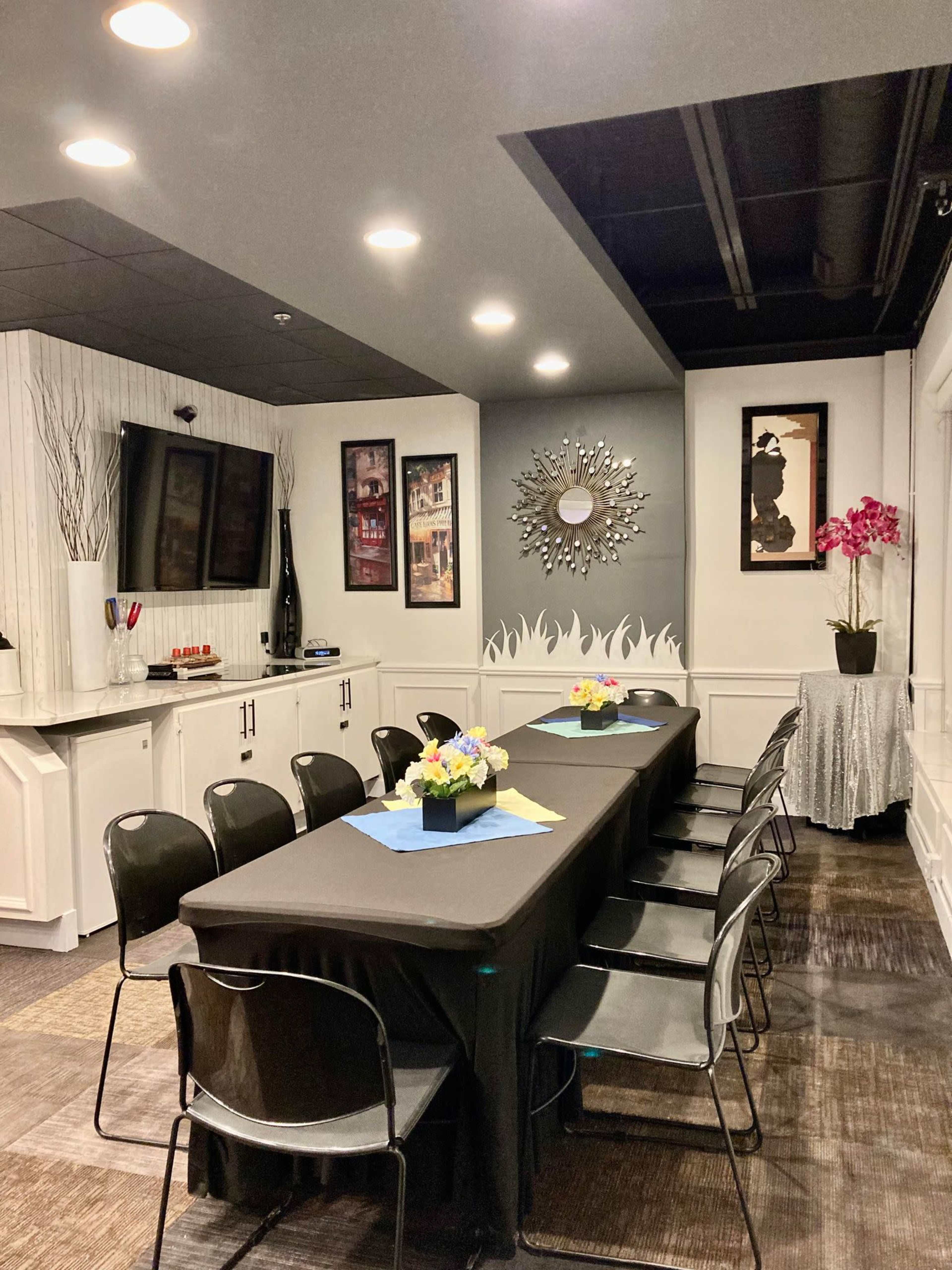 A conference room features a long table with black coverings and seating, accented by floral centerpieces, framed artwork on the walls, and a large mirror.